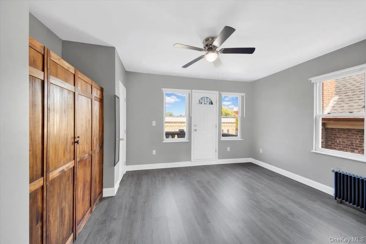 Unfurnished bedroom with a closet, dark wood finished floors, ceiling fan, and radiator heating unit Unfurnished bedroom with a closet, dark wood finished floors, ceiling fan, and radiator heating unit