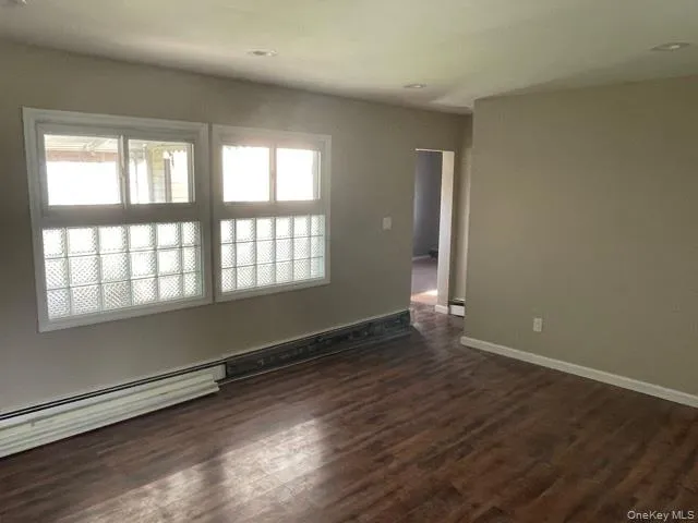 Unfurnished room featuring dark wood-style floors and a baseboard radiator Unfurnished room featuring dark wood-style floors and a baseboard radiator