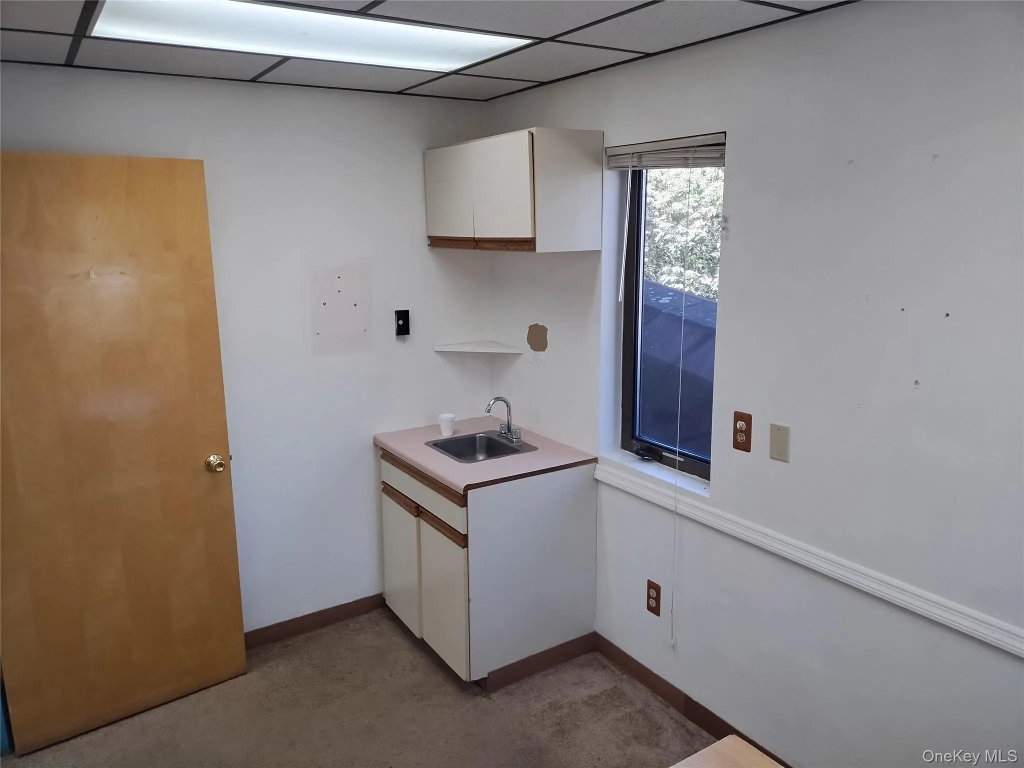 Kitchen featuring white cabinets, light countertops, a drop ceiling, and light carpet Kitchen featuring white cabinets, light countertops, a drop ceiling, and light carpet