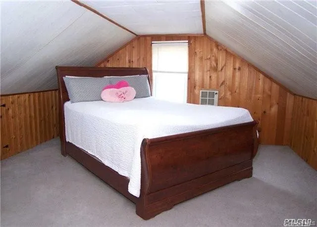 Bedroom with wooden walls, lofted ceiling, and light colored carpet Bedroom with wooden walls, lofted ceiling, and light colored carpet