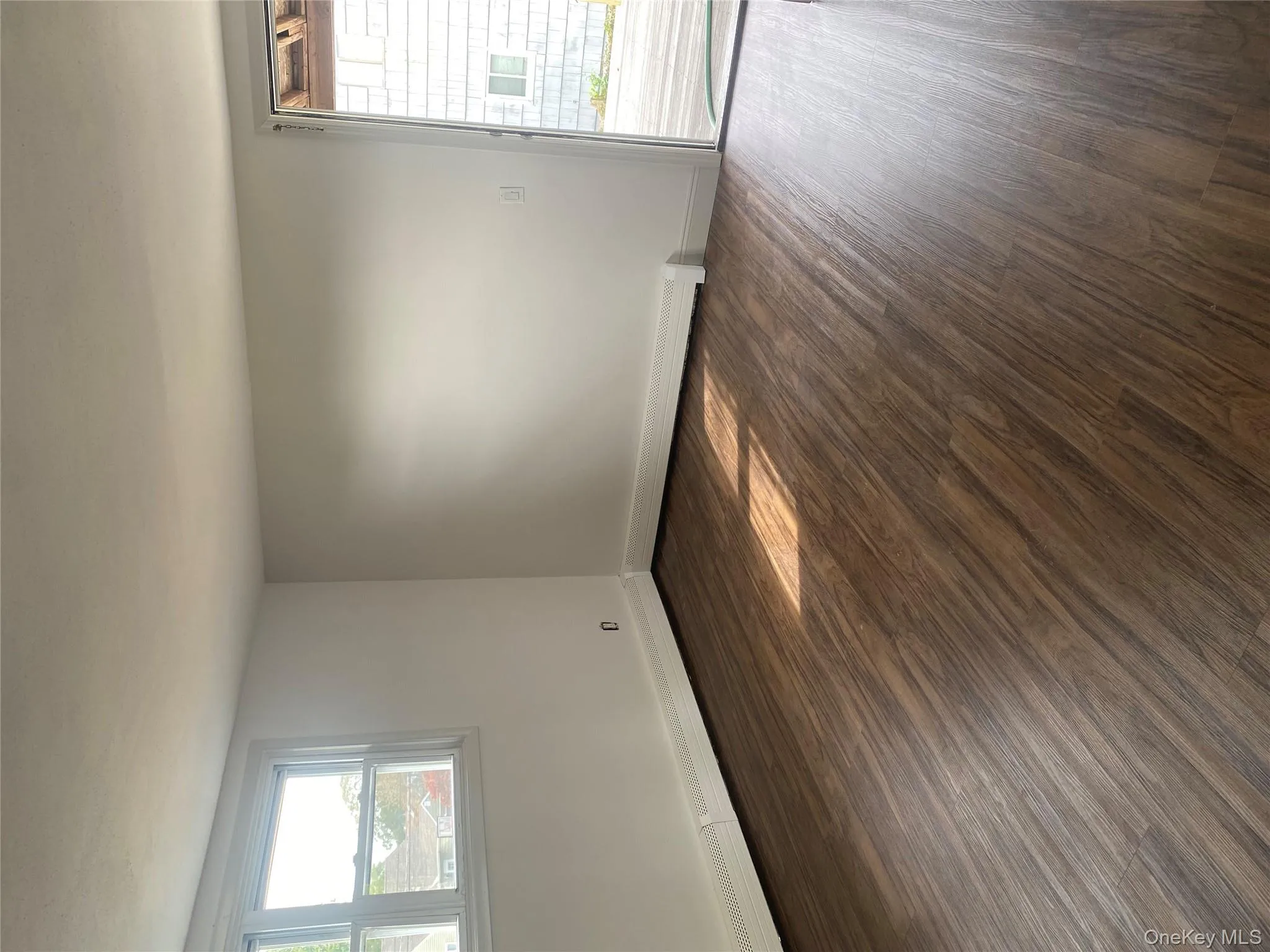Empty room with healthy amount of natural light, dark wood-type flooring, and baseboard heating Empty room with healthy amount of natural light, dark wood-type flooring, and baseboard heating