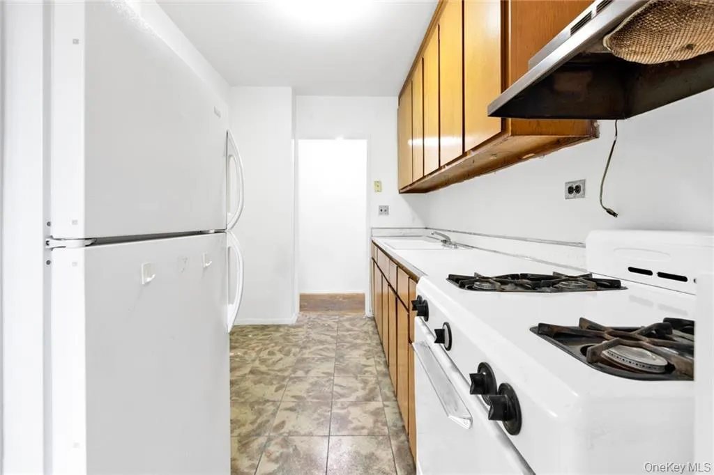 Kitchen featuring brown cabinetry, light countertops, white appliances, under cabinet range hood, and light tile patterned floors Kitchen featuring brown cabinetry, light countertops, white appliances, under cabinet range hood, and light tile patterned floors