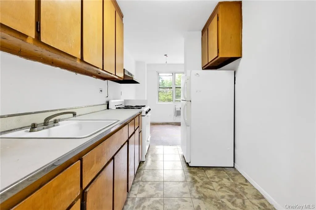 Kitchen with brown cabinetry, white appliances, light countertops, and light tile patterned flooring Kitchen with brown cabinetry, white appliances, light countertops, and light tile patterned flooring