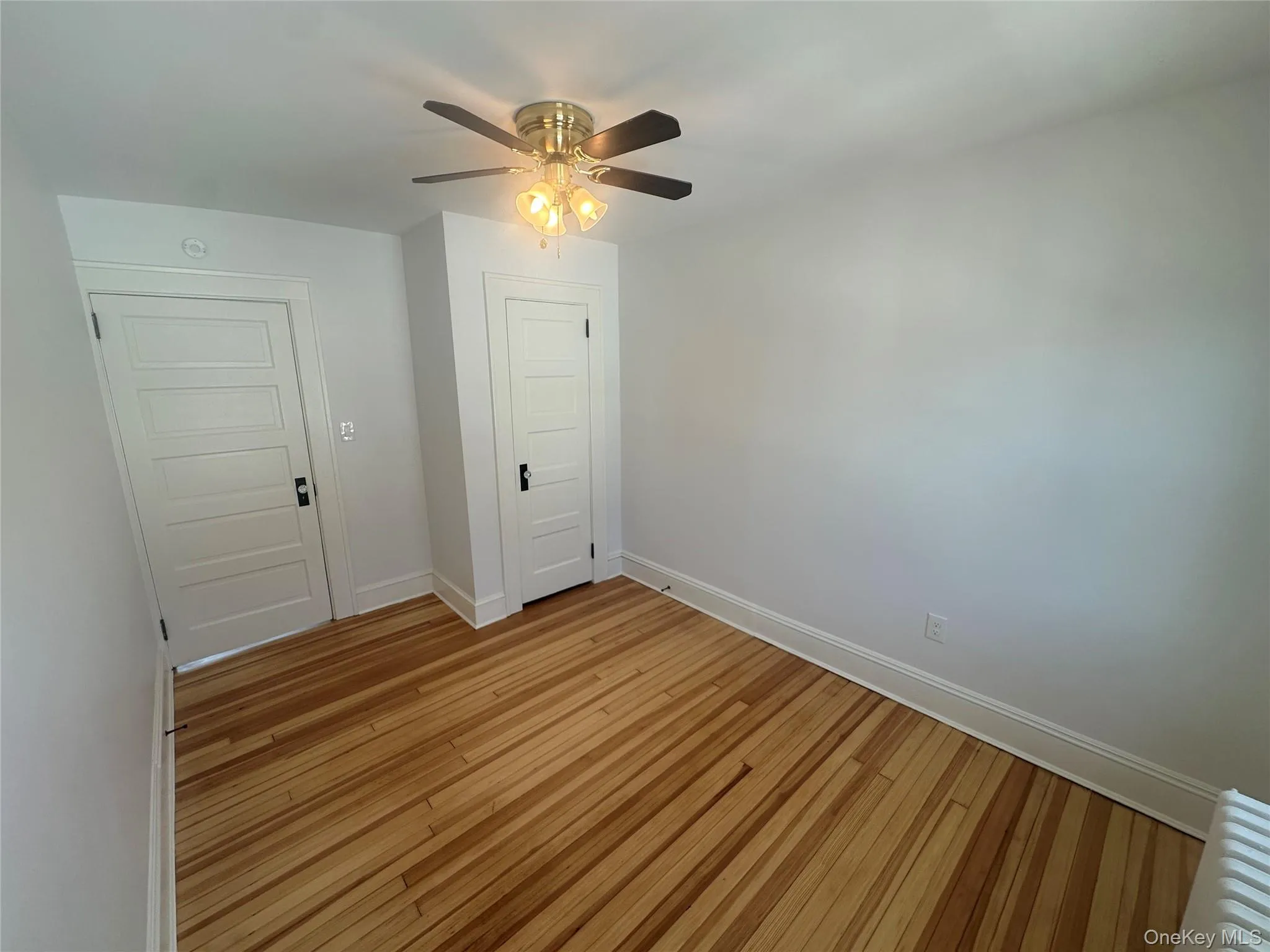 Empty room with light wood-type flooring, radiator, and a ceiling fan Empty room with light wood-type flooring, radiator, and a ceiling fan