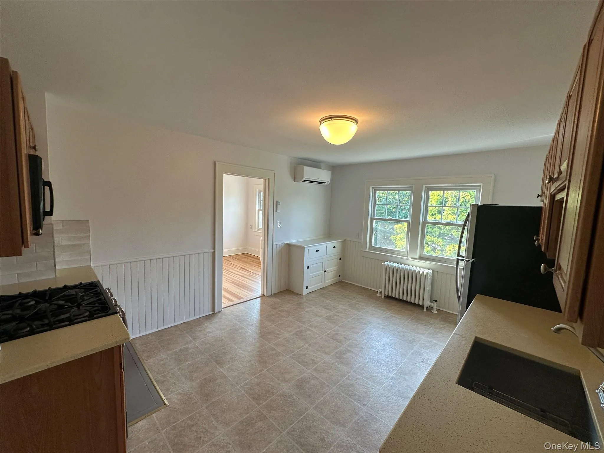 Kitchen with brown cabinets, radiator, a wainscoted wall, black appliances, and light stone countertops Kitchen with brown cabinets, radiator, a wainscoted wall, black appliances, and light stone countertops