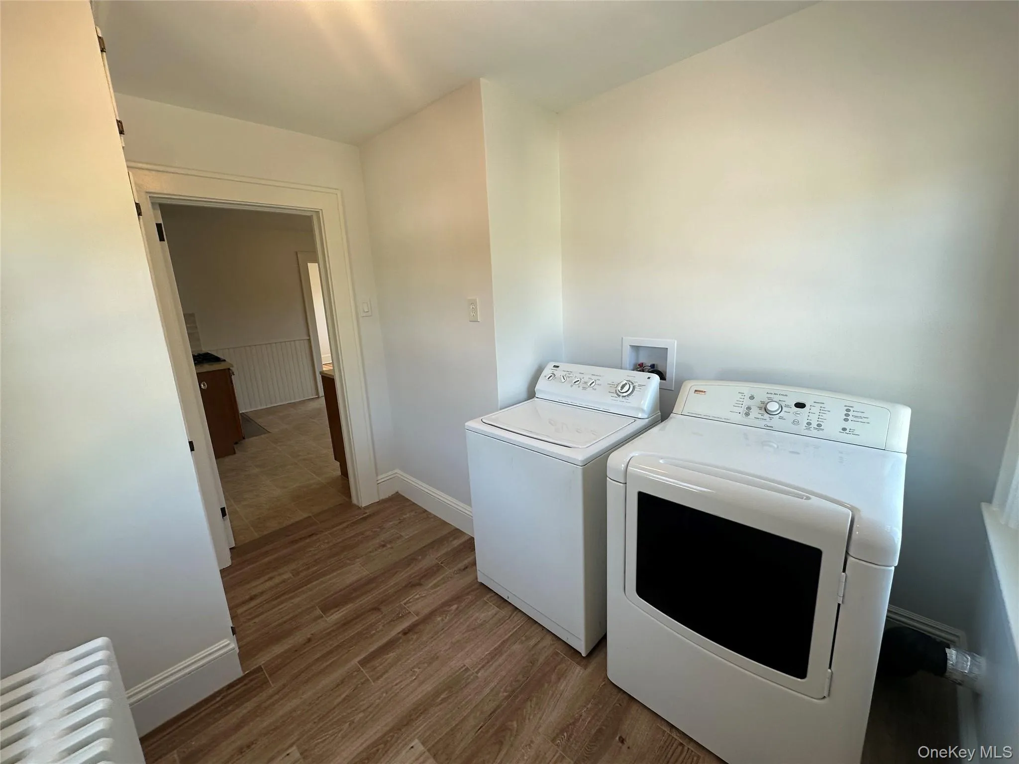 Washroom with radiator, light wood finished floors, and washer and clothes dryer Washroom with radiator, light wood finished floors, and washer and clothes dryer