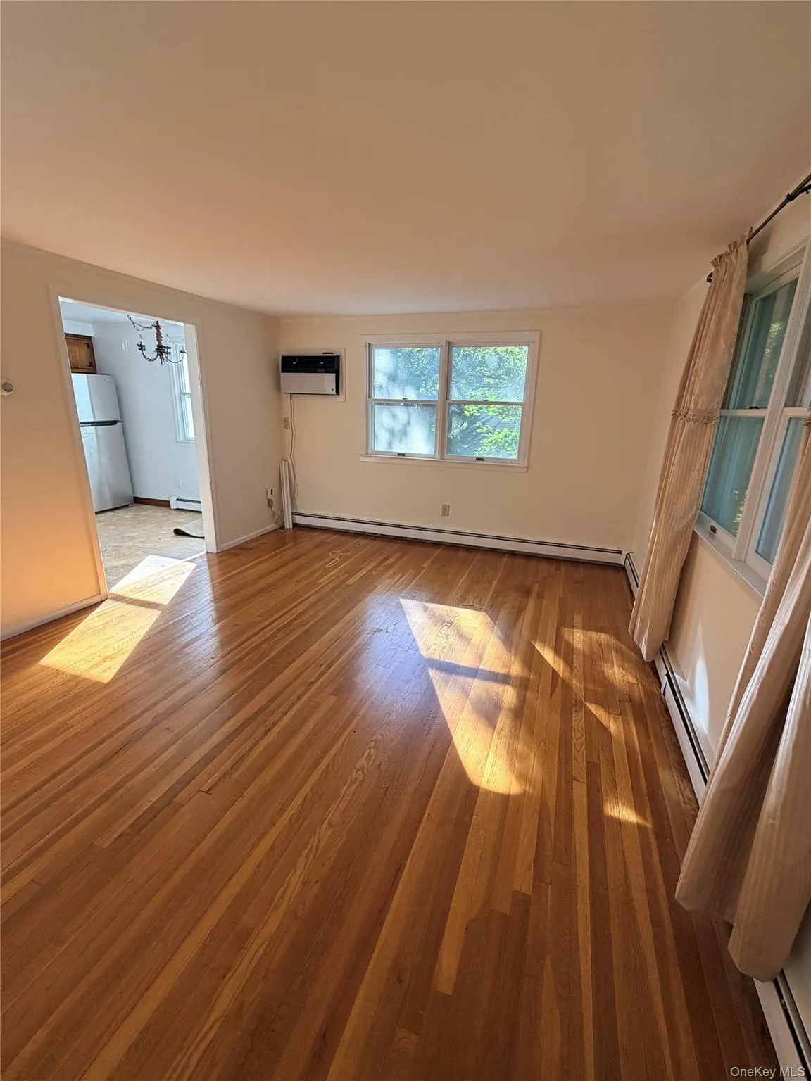 Unfurnished living room featuring wood finished floors, a chandelier, a baseboard radiator, and a wall unit AC Unfurnished living room featuring wood finished floors, a chandelier, a baseboard radiator, and a wall unit AC