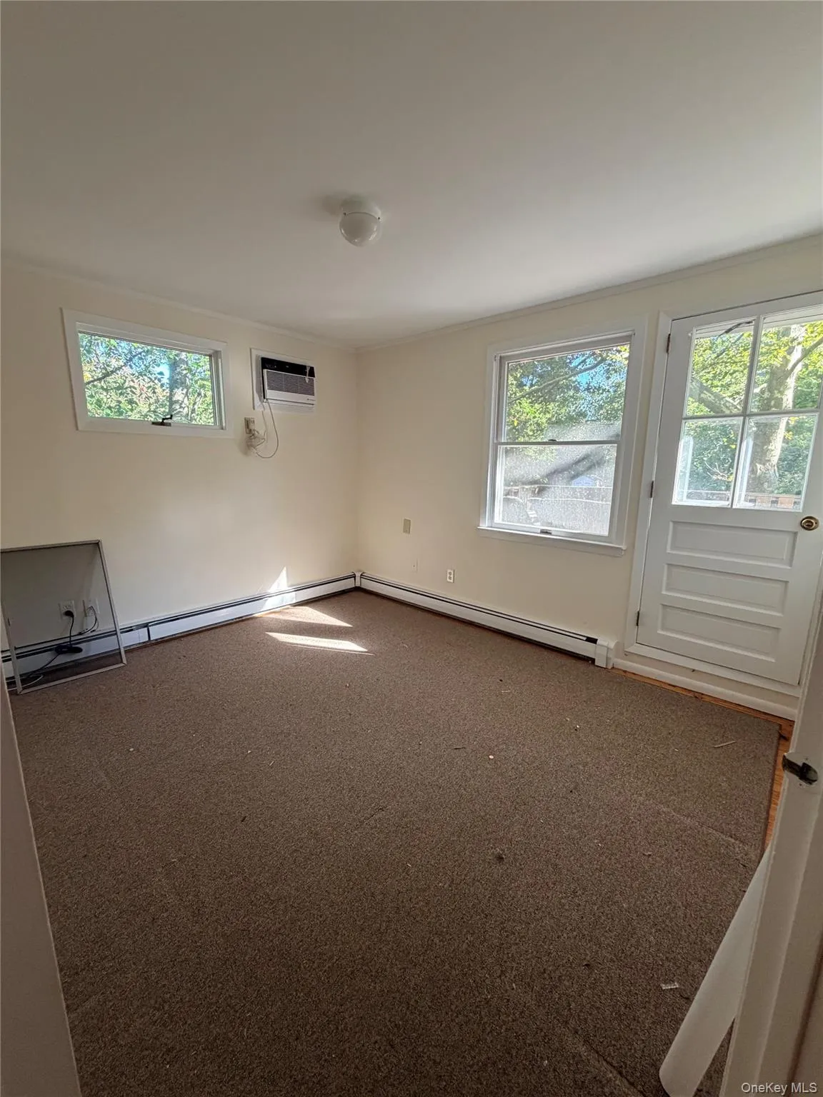 Carpeted empty room featuring plenty of natural light, a baseboard heating unit, and a wall unit AC Carpeted empty room featuring plenty of natural light, a baseboard heating unit, and a wall unit AC