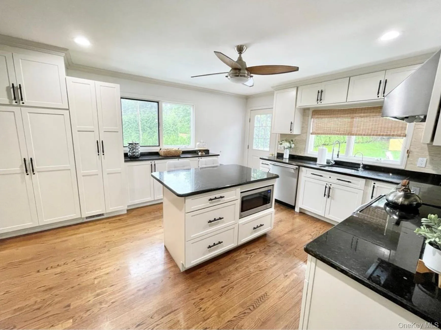 Kitchen with light wood-style floors, crown molding, ceiling fan, white cabinetry, and dark stone counters Kitchen with light wood-style floors, crown molding, ceiling fan, white cabinetry, and dark stone counters
