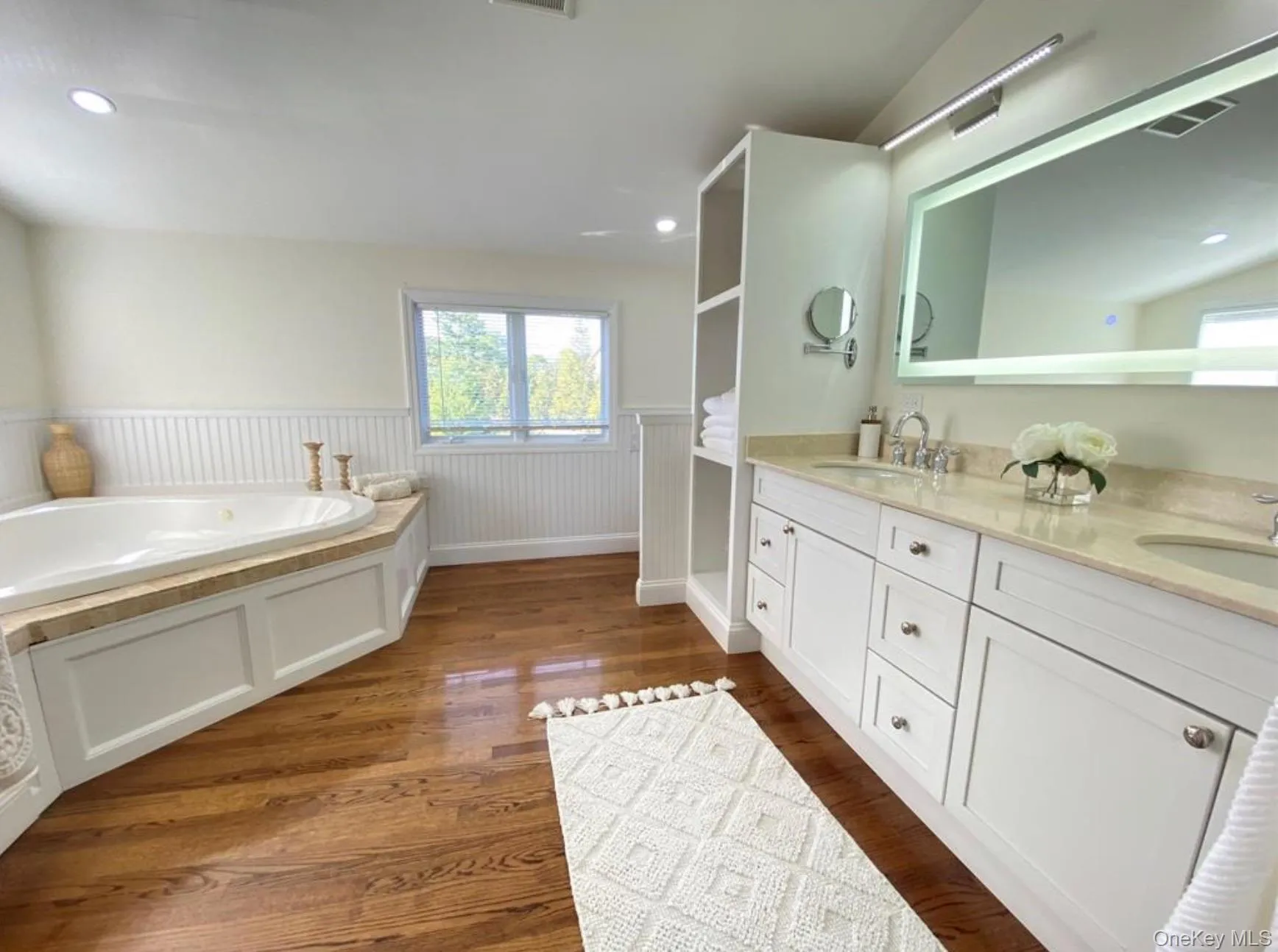 Bathroom with a wainscoted wall, a bath, double vanity, recessed lighting, and dark wood finished floors Bathroom with a wainscoted wall, a bath, double vanity, recessed lighting, and dark wood finished floors