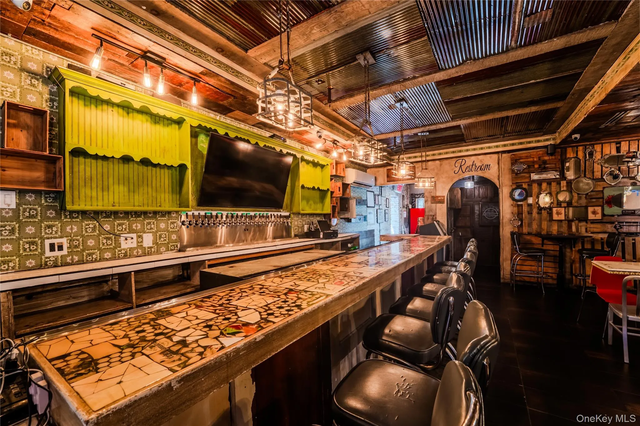 Indoor dry bar with green cabinetry, arched walkways, decorative light fixtures, backsplash, and beamed ceiling Indoor dry bar with green cabinetry, arched walkways, decorative light fixtures, backsplash, and beamed ceiling