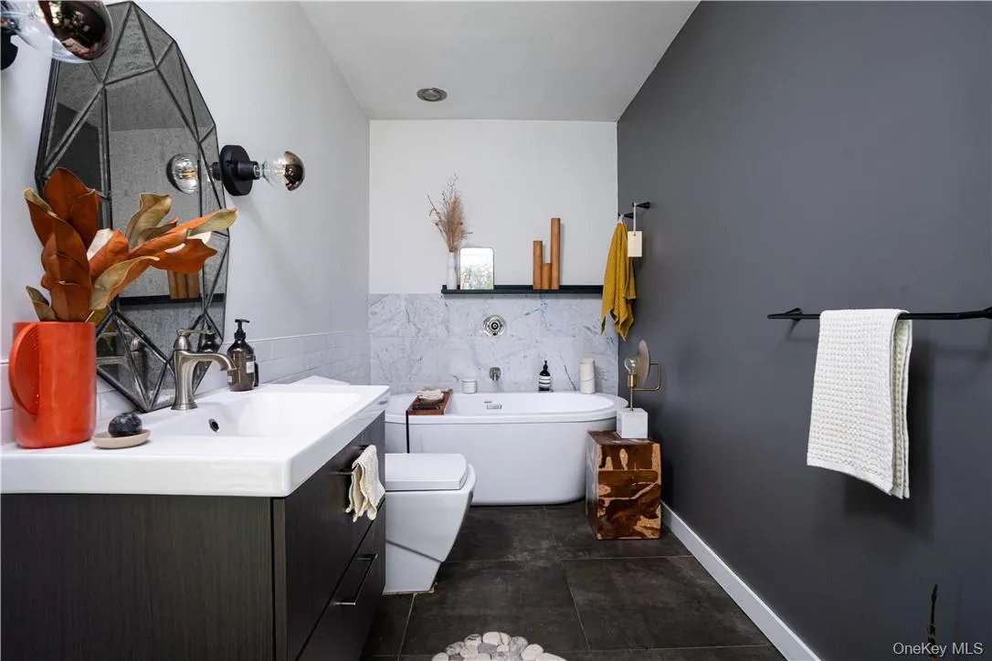 Bathroom featuring tile patterned flooring, a bathtub, toilet, vanity, and tile walls Bathroom featuring tile patterned flooring, a bathtub, toilet, vanity, and tile walls