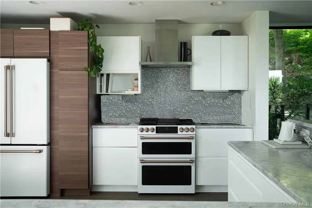 Kitchen featuring premium appliances, backsplash, white cabinetry, and wall chimney range hood Kitchen featuring premium appliances, backsplash, white cabinetry, and wall chimney range hood