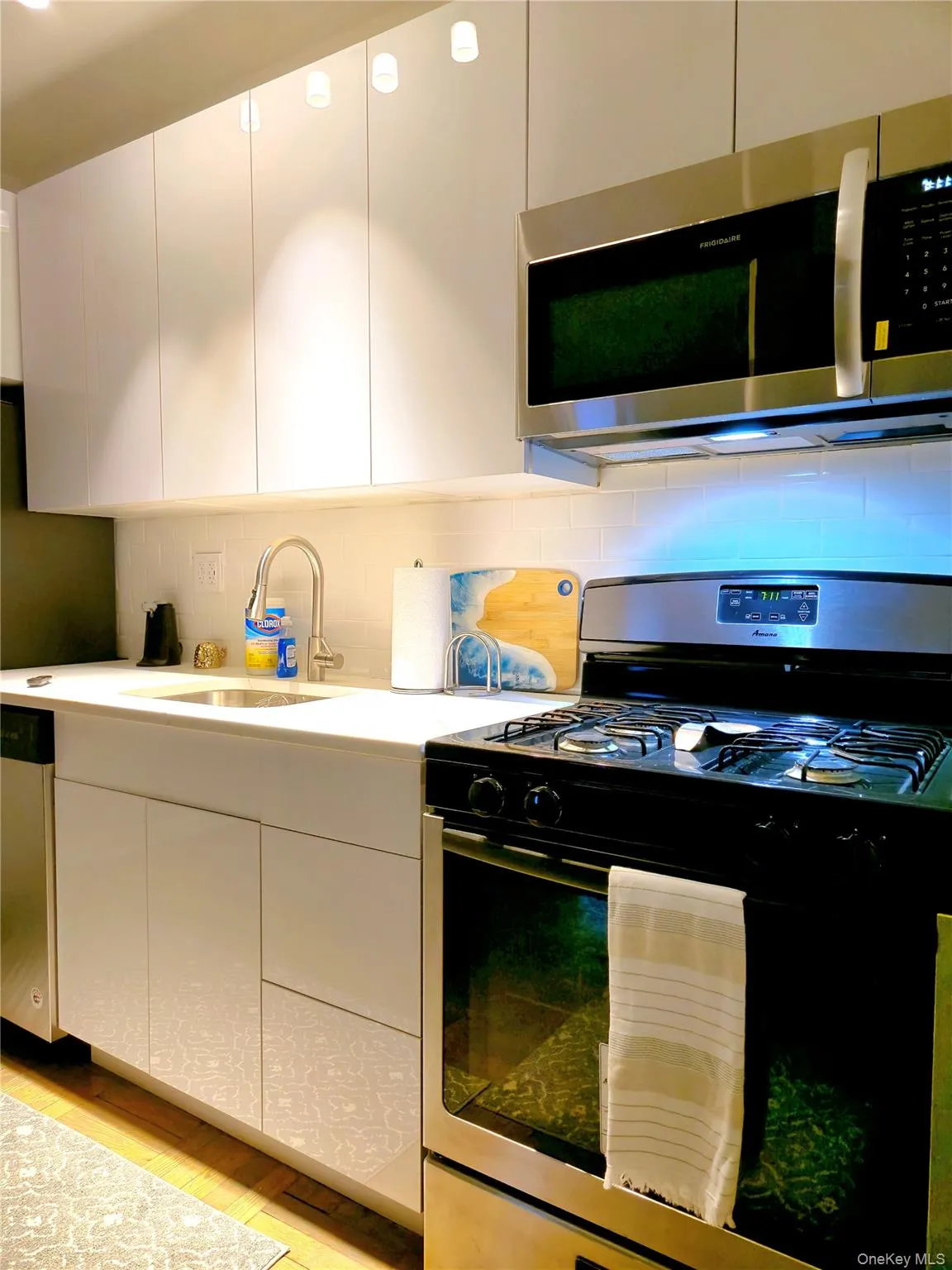 Kitchen featuring light wood-style floors, tasteful backsplash, white cabinetry, appliances with stainless steel finishes, and a sink Kitchen featuring light wood-style floors, tasteful backsplash, white cabinetry, appliances with stainless steel finishes, and a sink