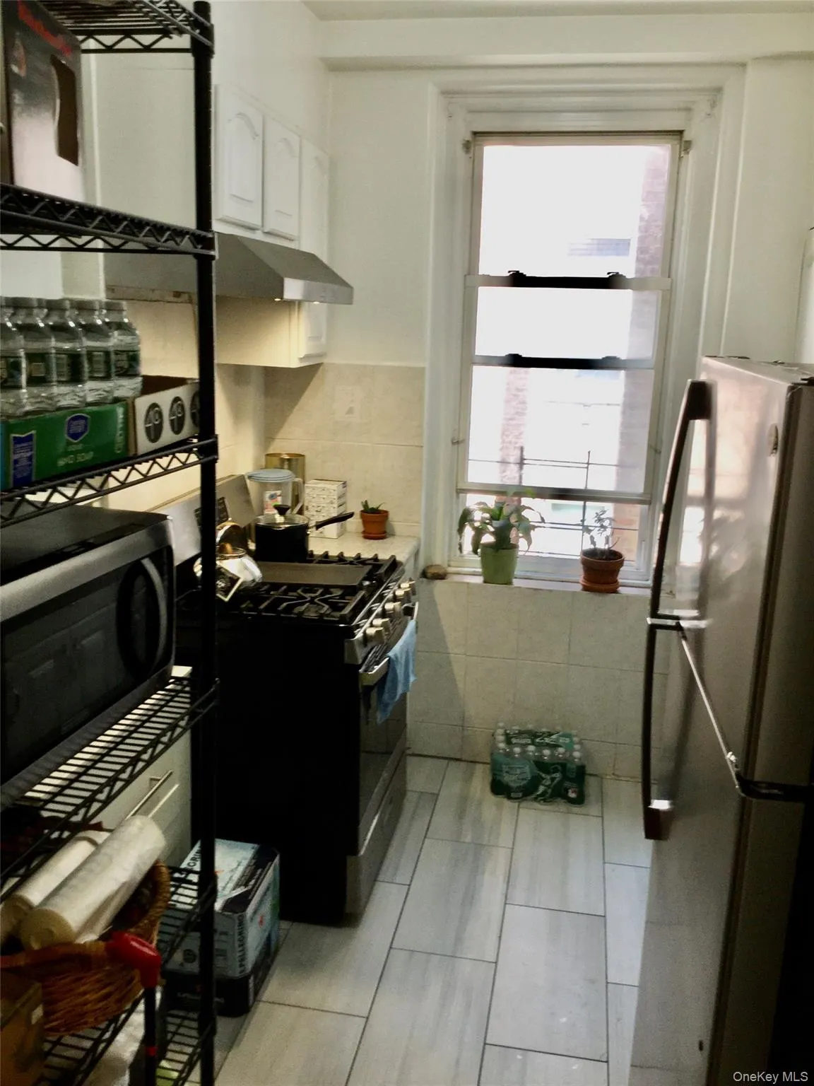 Kitchen with white cabinets, stainless steel appliances, light countertops, under cabinet range hood, and light tile patterned floors Kitchen with white cabinets, stainless steel appliances, light countertops, under cabinet range hood, and light tile patterned floors
