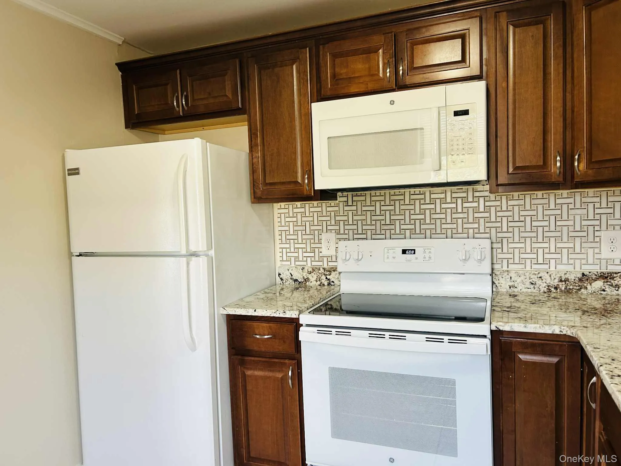 Kitchen with white appliances, decorative backsplash, light stone countertops, dark brown cabinets, and ornamental molding Kitchen with white appliances, decorative backsplash, light stone countertops, dark brown cabinets, and ornamental molding