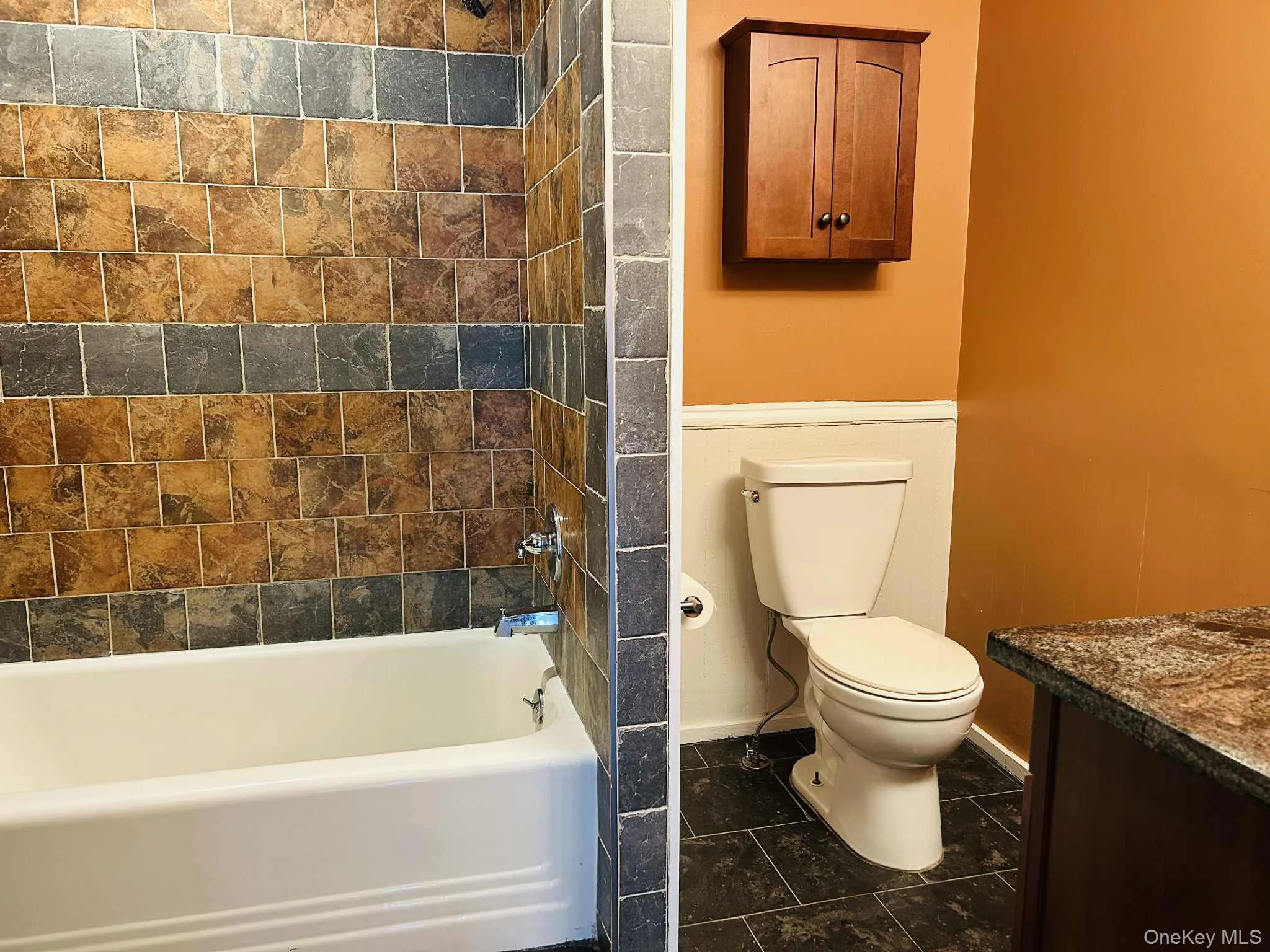 Bathroom featuring washtub / shower combination, vanity, and dark tile patterned flooring Bathroom featuring washtub / shower combination, vanity, and dark tile patterned flooring