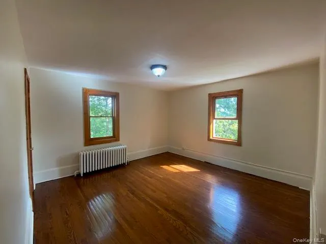 Unfurnished room featuring radiator heating unit, dark wood-style flooring, and plenty of natural light Unfurnished room featuring radiator heating unit, dark wood-style flooring, and plenty of natural light
