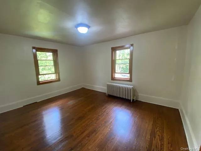 Spare room featuring radiator heating unit and dark wood-style flooring Spare room featuring radiator heating unit and dark wood-style flooring