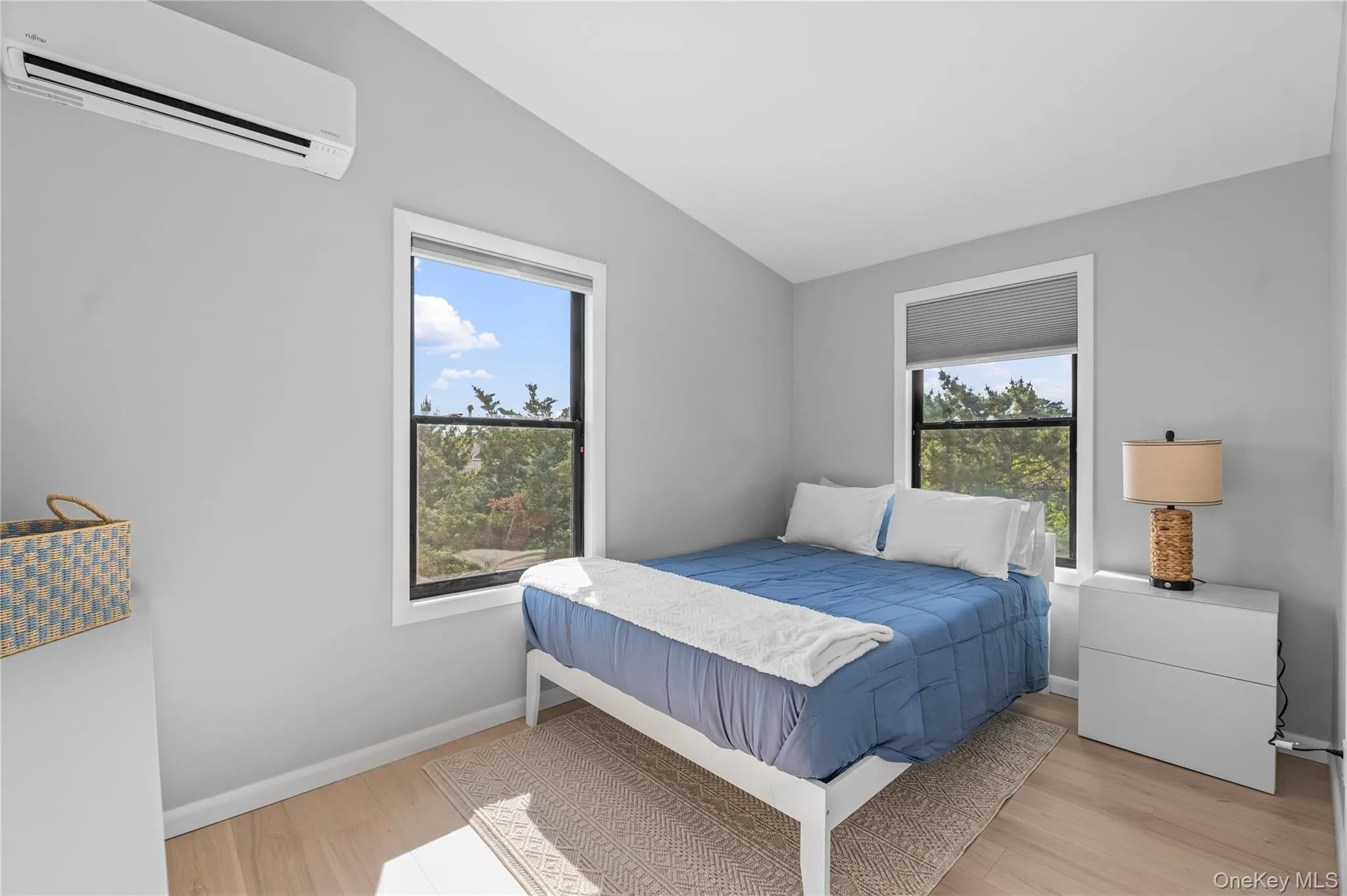 Bedroom with an AC wall unit, vaulted ceiling, light wood finished floors, and multiple windows Bedroom with an AC wall unit, vaulted ceiling, light wood finished floors, and multiple windows