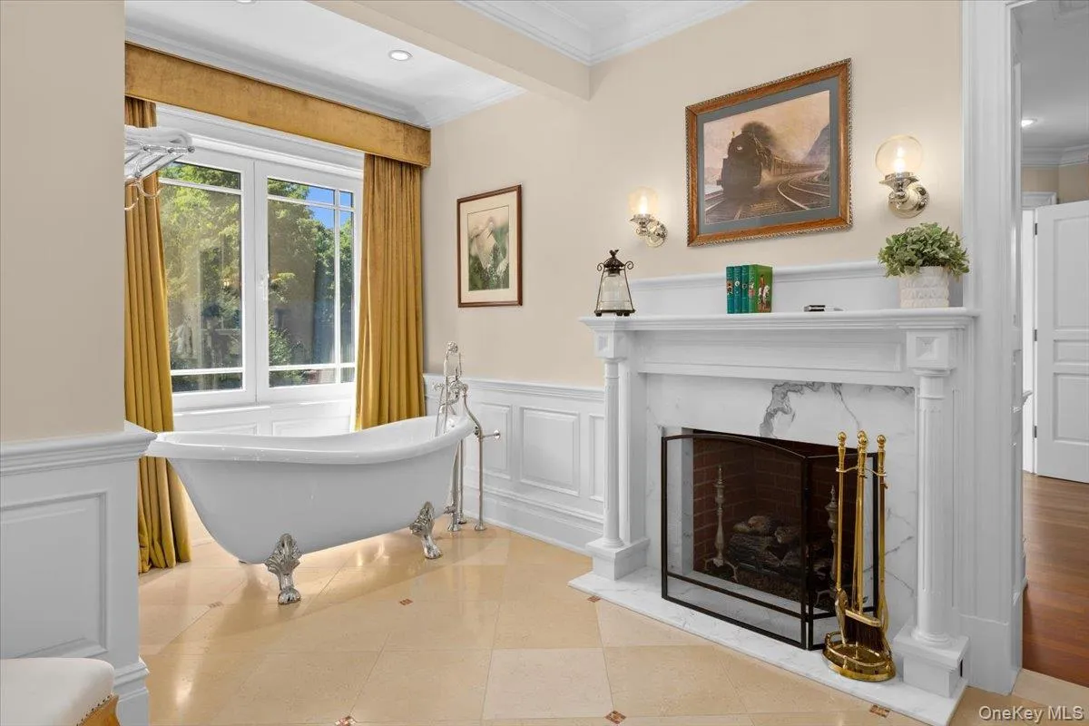 Full bathroom with a soaking tub, ornamental molding, a fireplace, a decorative wall, and a wainscoted wall Full bathroom with a soaking tub, ornamental molding, a fireplace, a decorative wall, and a wainscoted wall