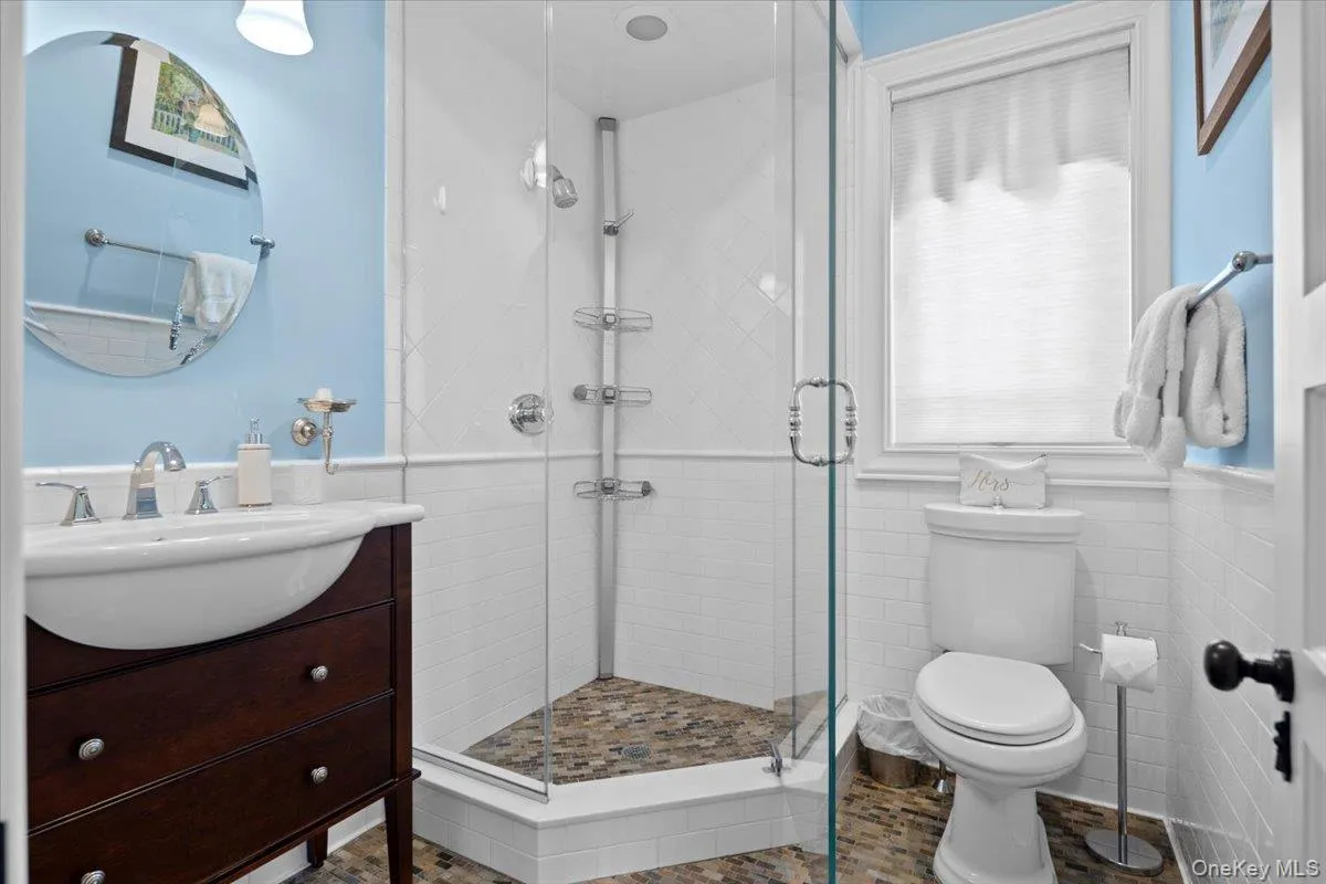 Full bath featuring tile walls, healthy amount of natural light, a wainscoted wall, a shower stall, and vanity Full bath featuring tile walls, healthy amount of natural light, a wainscoted wall, a shower stall, and vanity