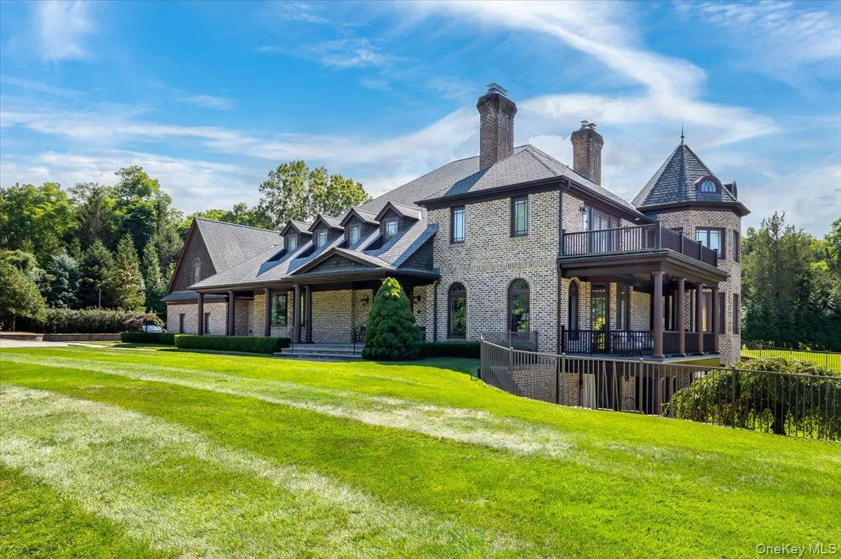 View of front of property with brick siding, a front yard, a chimney, and a balcony View of front of property with brick siding, a front yard, a chimney, and a balcony