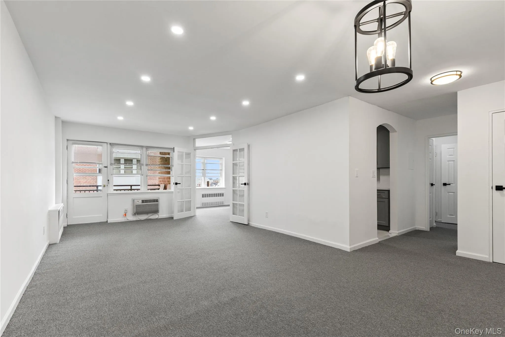 Unfurnished living room with recessed lighting, dark colored carpet, arched walkways, and radiator heating unit Unfurnished living room with recessed lighting, dark colored carpet, arched walkways, and radiator heating unit