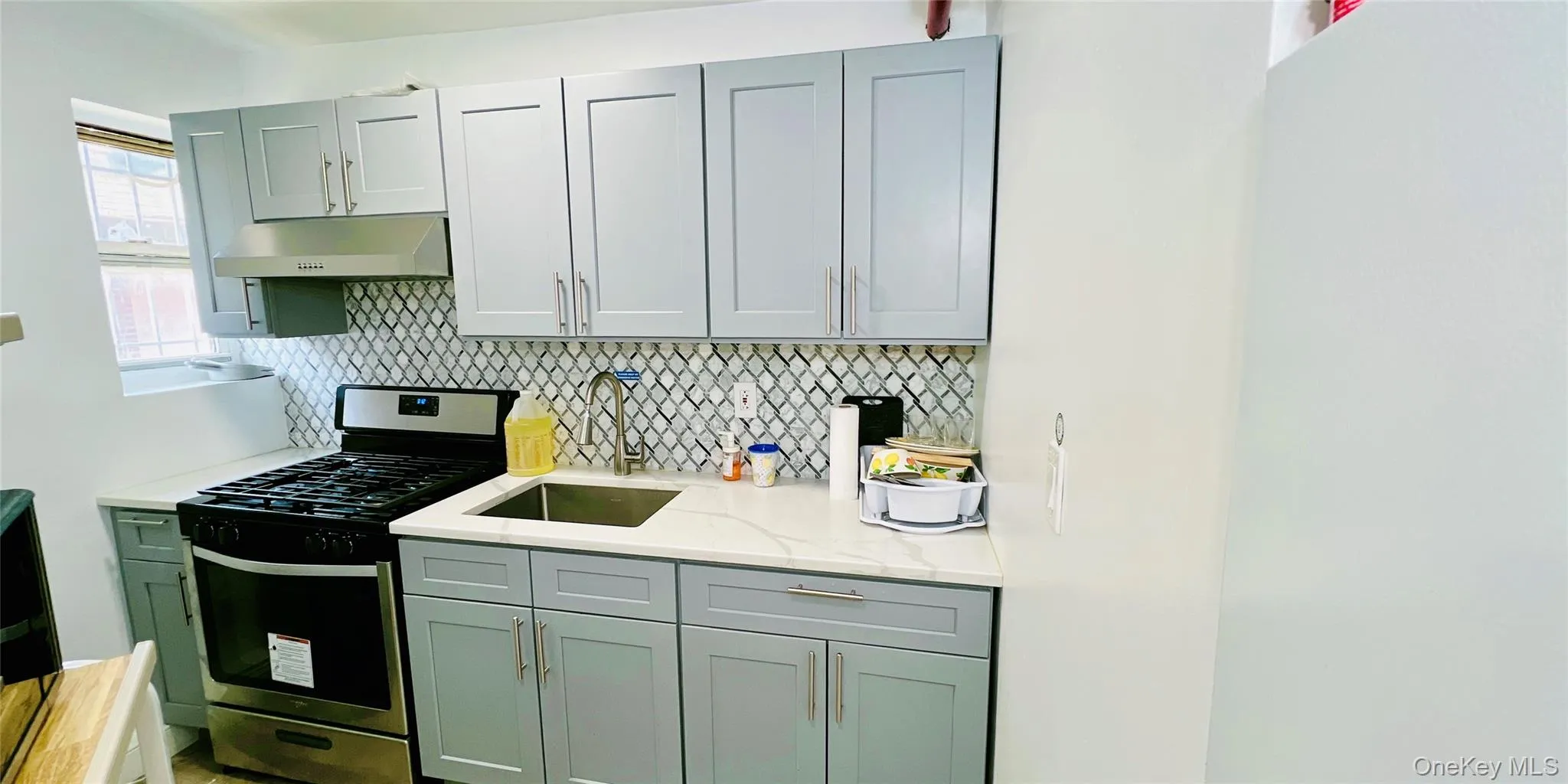 Kitchen featuring stainless steel gas range, backsplash, light stone counters, and under cabinet range hood Kitchen featuring stainless steel gas range, backsplash, light stone counters, and under cabinet range hood