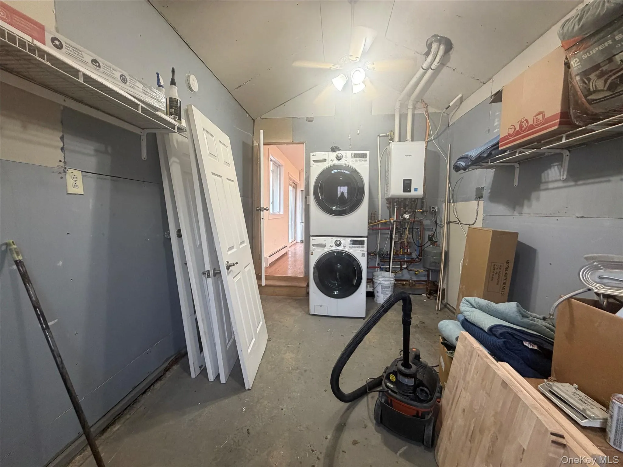 Laundry area with concrete floors, stacked washer and clothes dryer, a ceiling fan, and tankless water heater Laundry area with concrete floors, stacked washer and clothes dryer, a ceiling fan, and tankless water heater