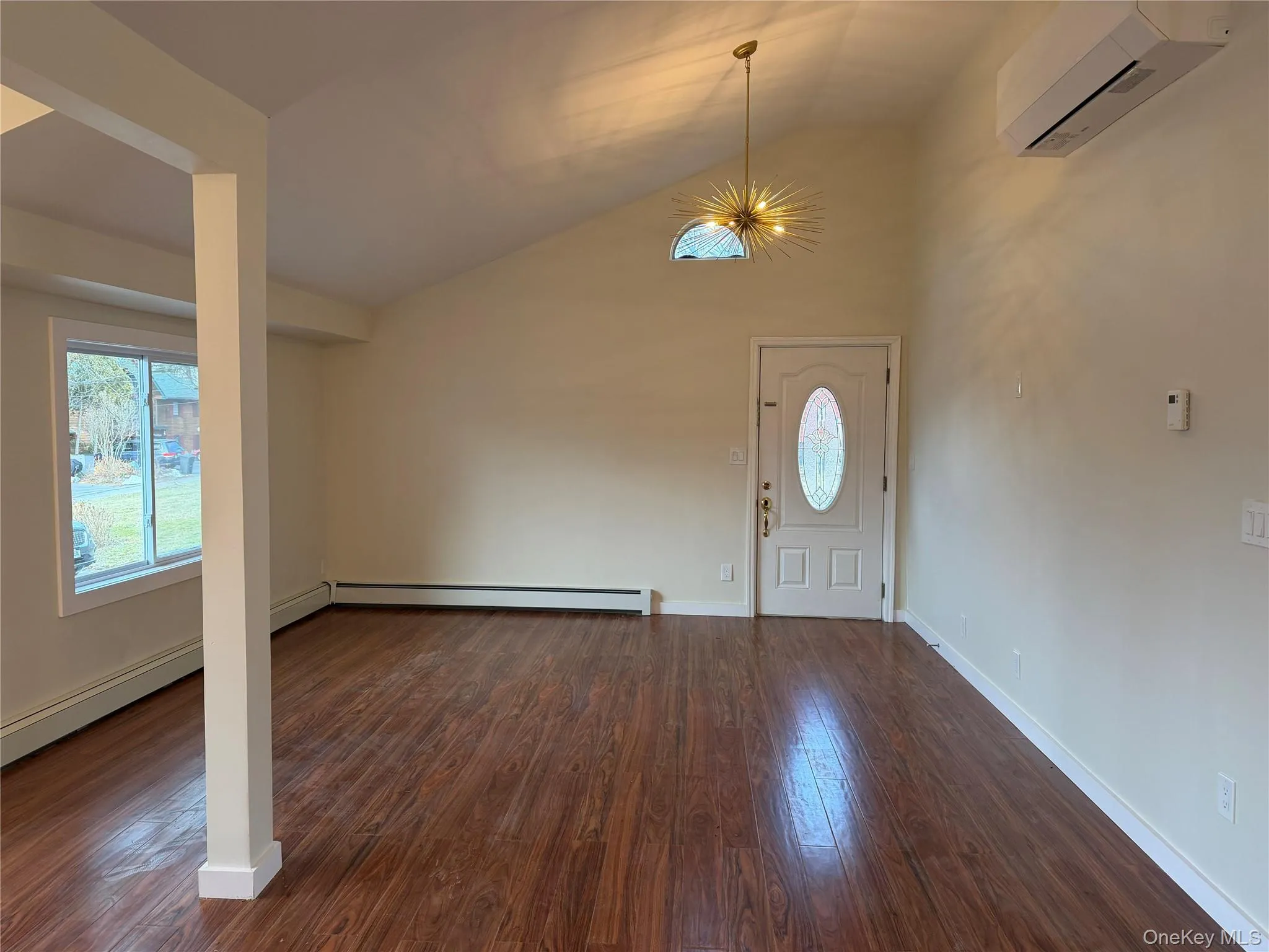 Foyer entrance featuring dark wood-style floors, a wall mounted AC, a chandelier, high vaulted ceiling, and baseboard heating Foyer entrance featuring dark wood-style floors, a wall mounted AC, a chandelier, high vaulted ceiling, and baseboard heating