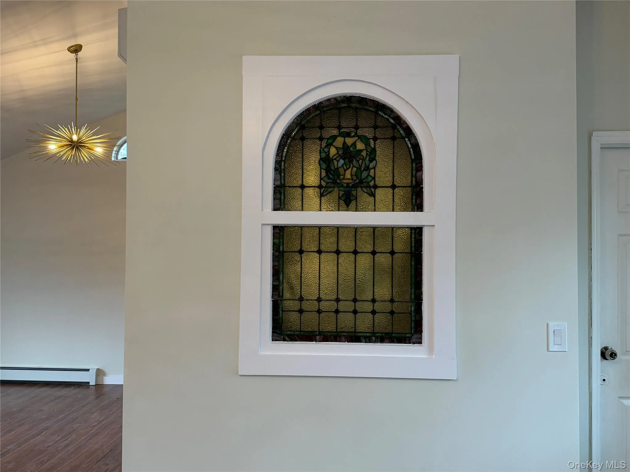 Detailed view of baseboard heating, stucco siding, and a chandelier Detailed view of baseboard heating, stucco siding, and a chandelier