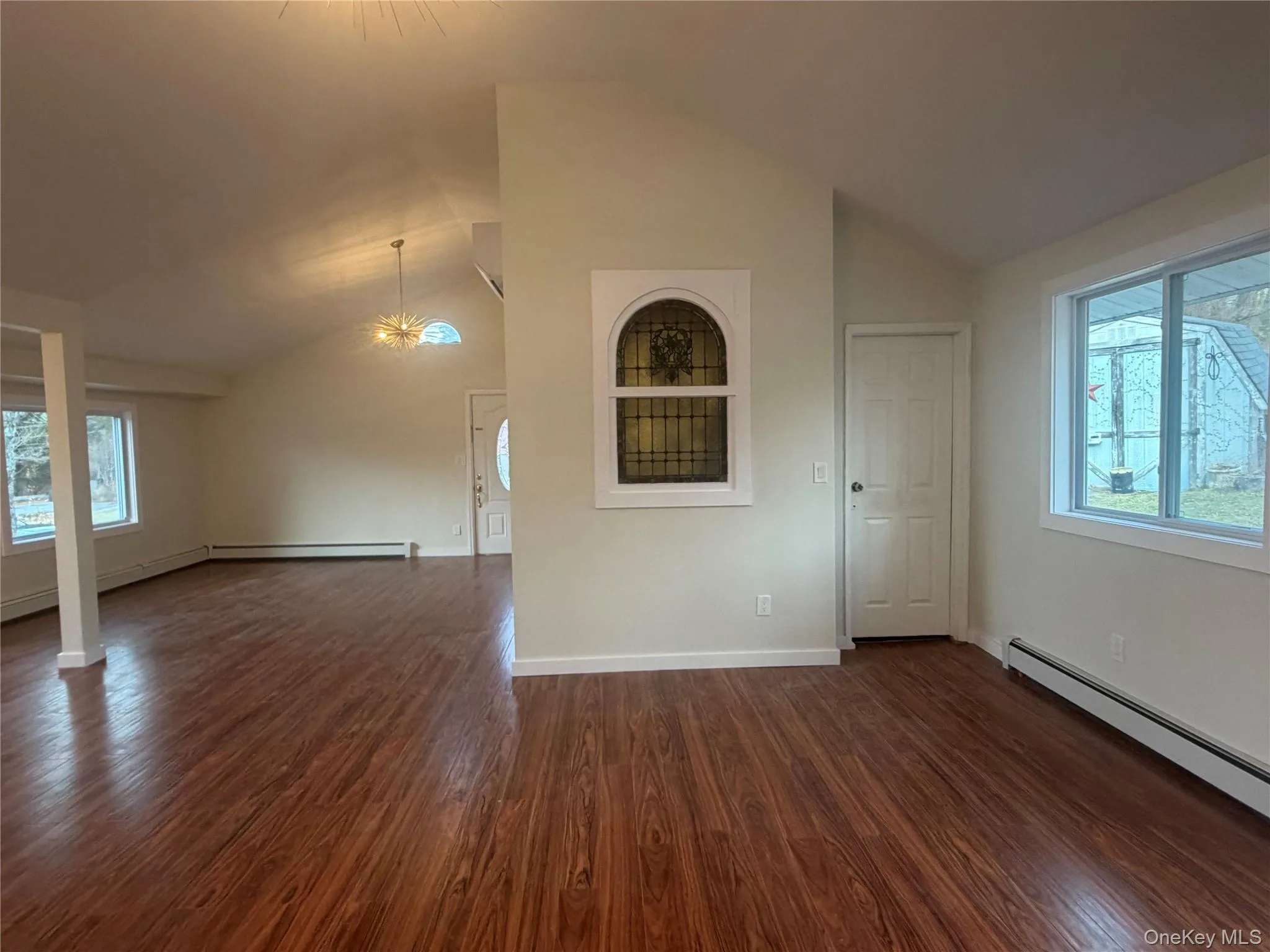 Spare room with lofted ceiling, a chandelier, dark wood-type flooring, and a baseboard heating unit Spare room with lofted ceiling, a chandelier, dark wood-type flooring, and a baseboard heating unit