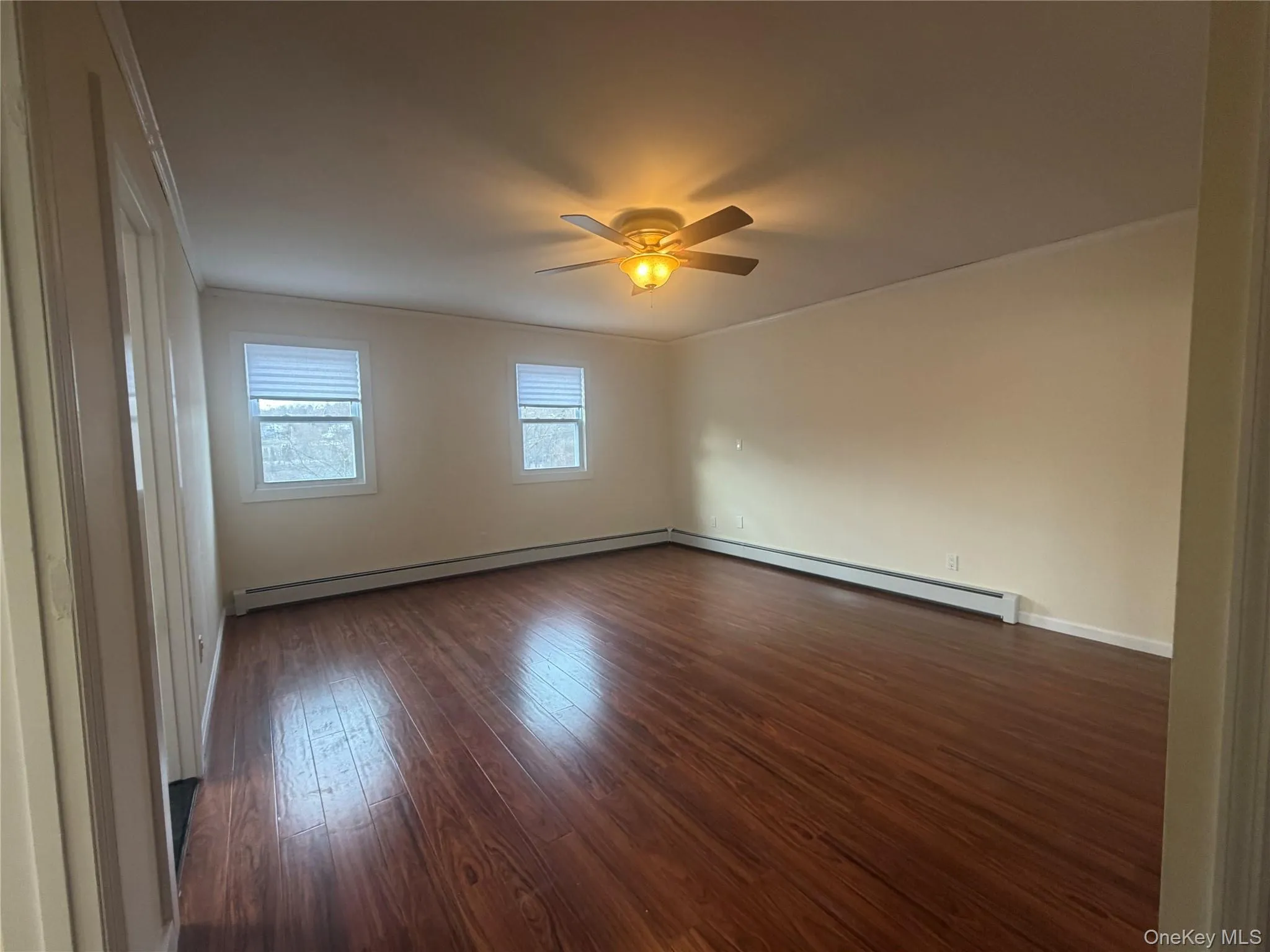 Unfurnished room featuring ornamental molding, dark wood-style floors, a baseboard radiator, and ceiling fan Unfurnished room featuring ornamental molding, dark wood-style floors, a baseboard radiator, and ceiling fan