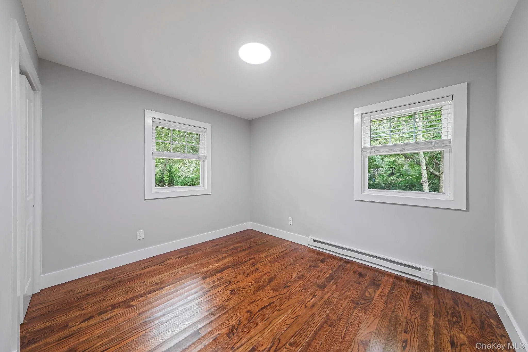 Unfurnished room with baseboard heating, healthy amount of natural light, and dark wood finished floors