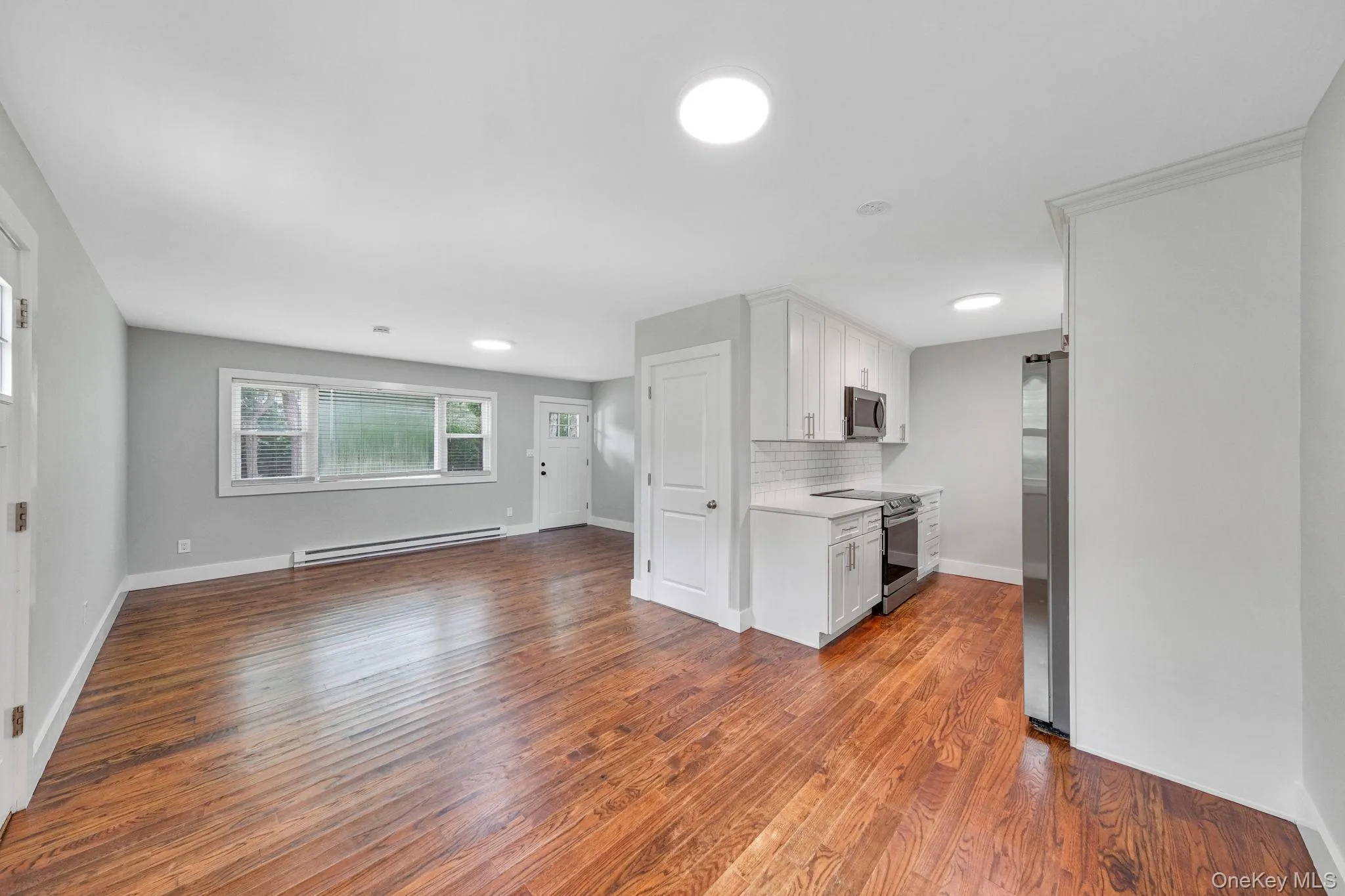 Kitchen with white cabinetry, appliances with stainless steel finishes, decorative backsplash, dark wood finished floors, and baseboard heating