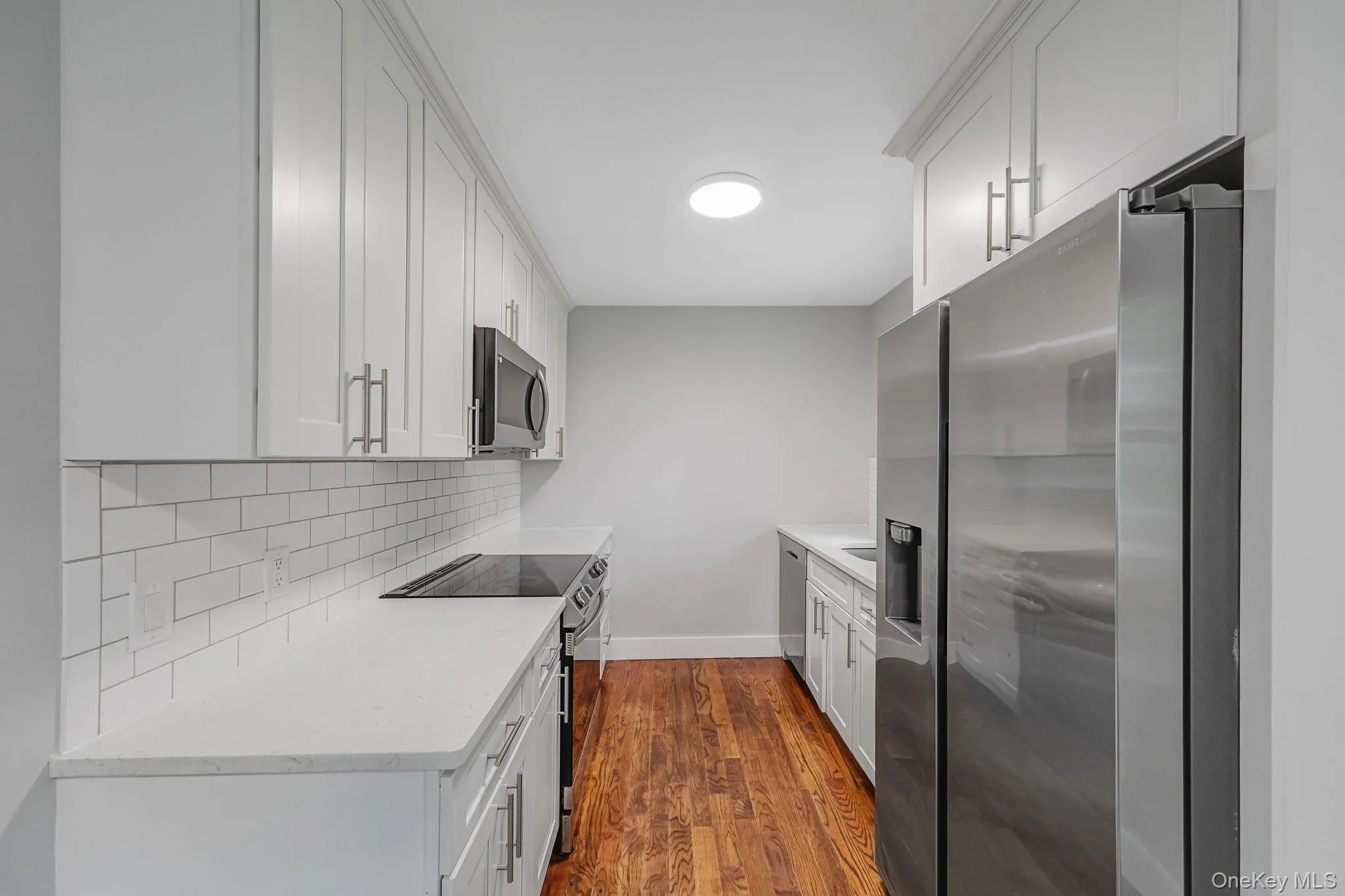 Kitchen with stainless steel appliances, white cabinets, dark wood-style flooring, light stone countertops, and backsplash