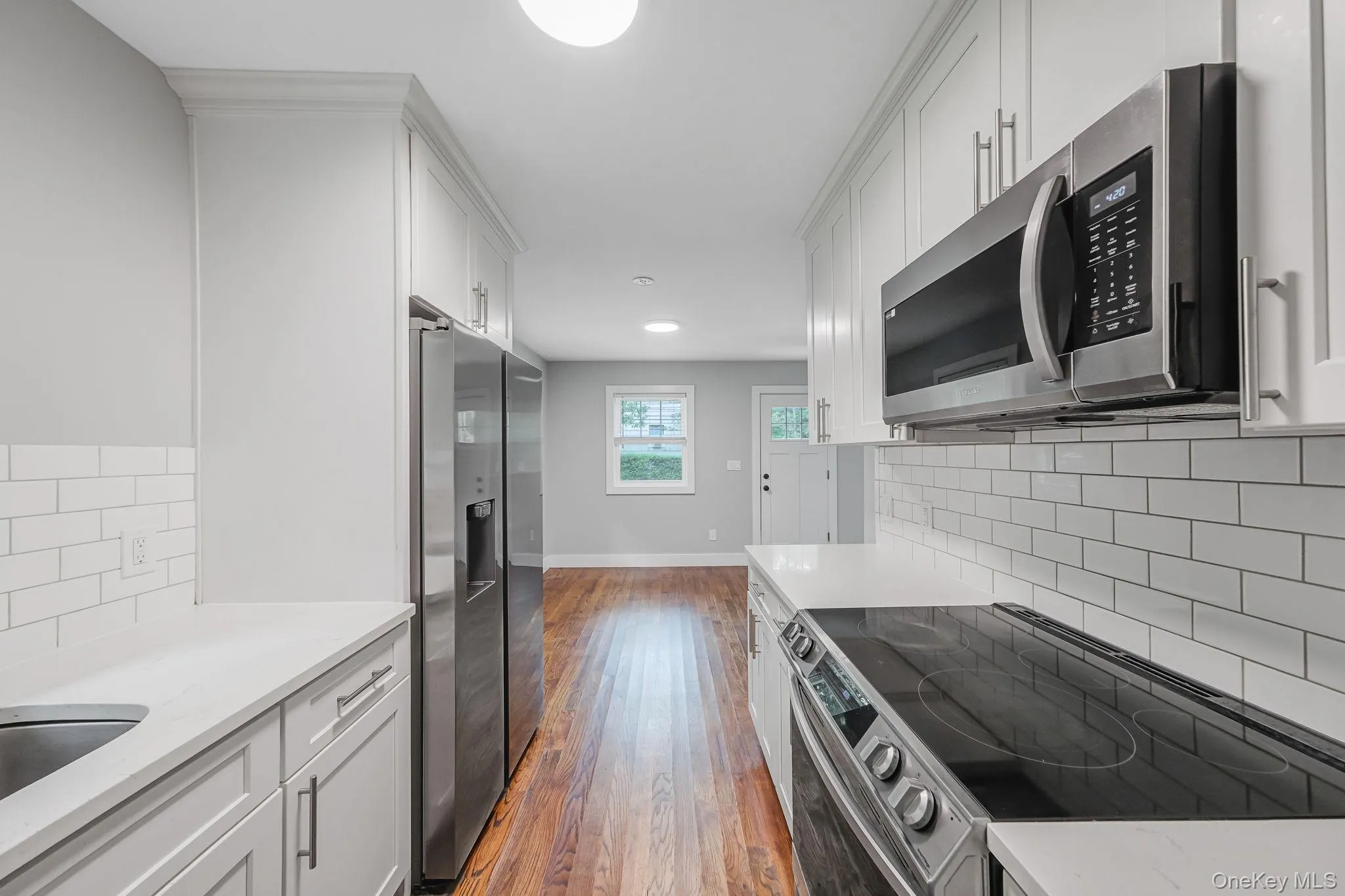 Kitchen featuring backsplash, appliances with stainless steel finishes, light stone counters, dark wood-style floors, and white cabinetry