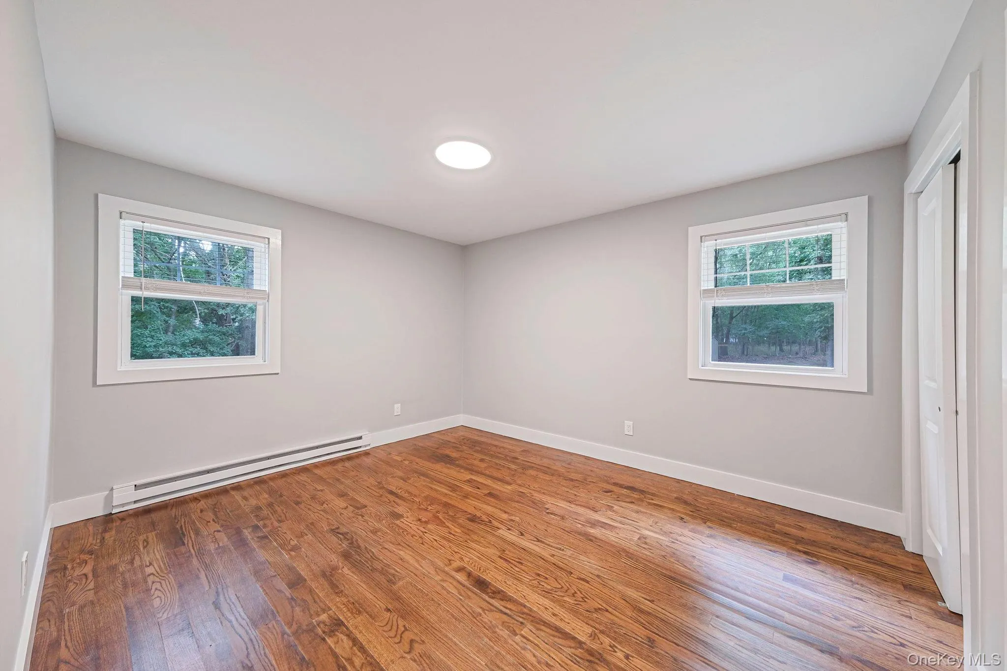 Unfurnished bedroom with baseboard heating, dark wood finished floors, and a closet