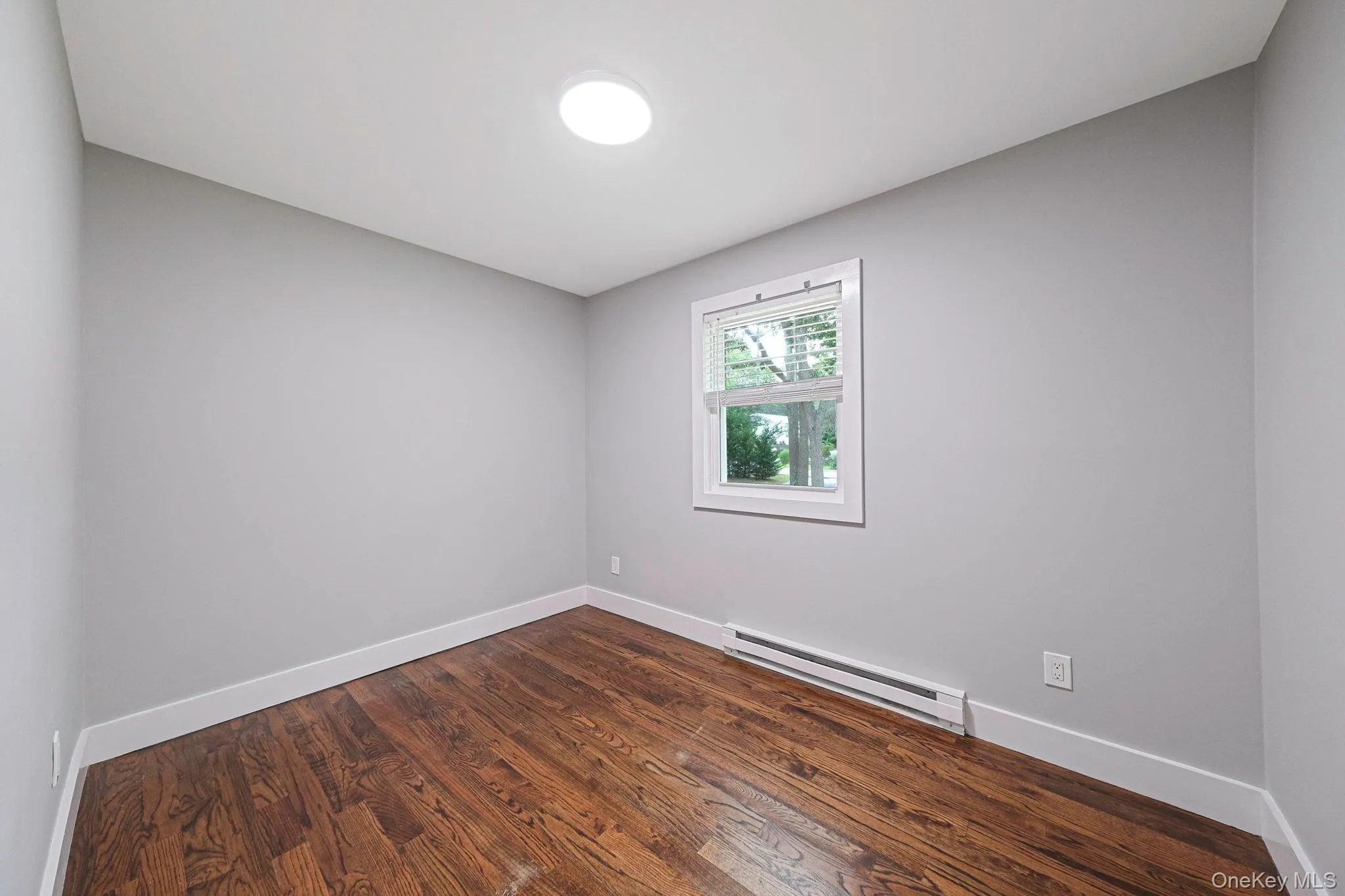 Empty room featuring a baseboard heating unit and dark wood-style flooring