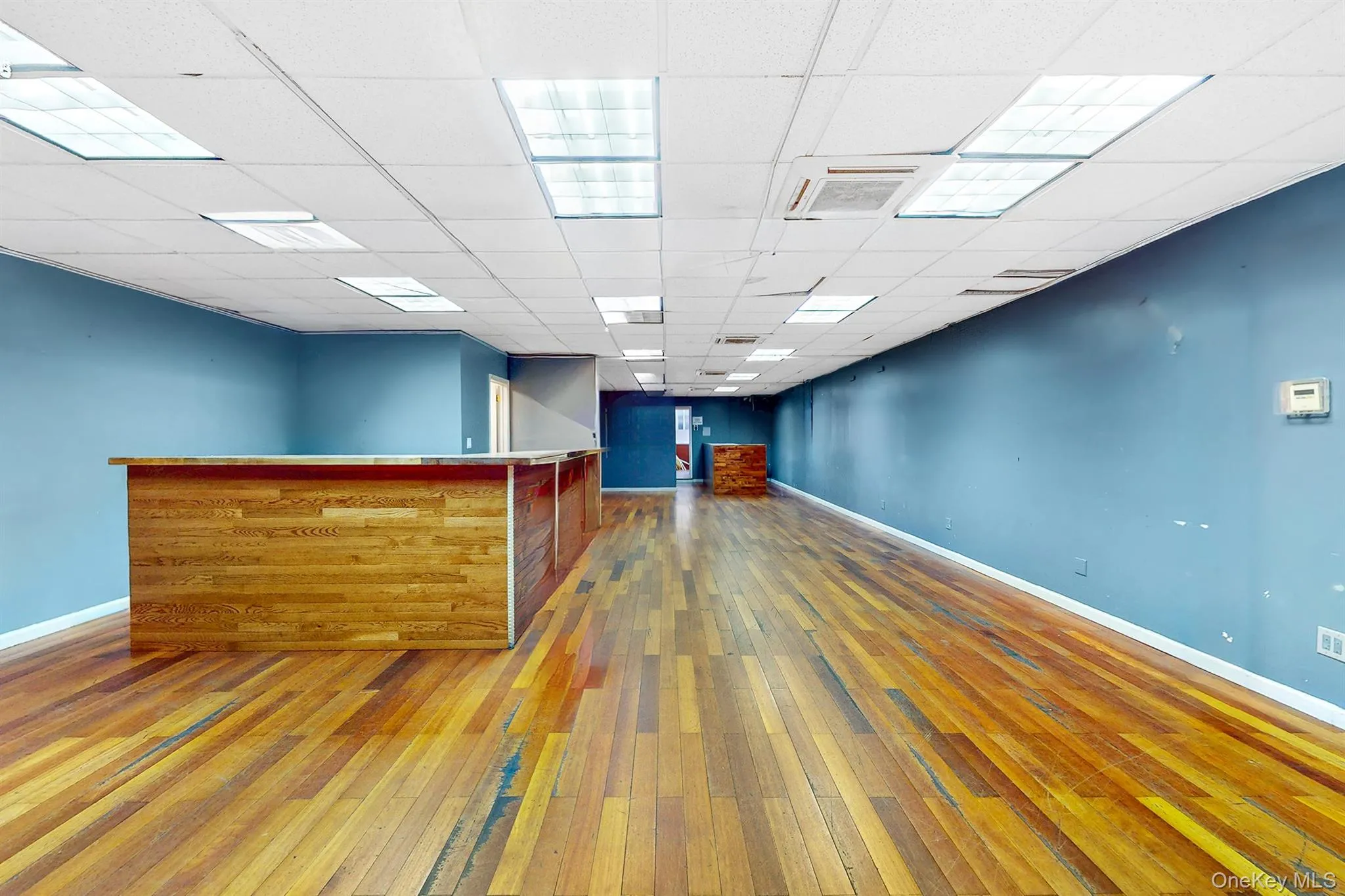 Unfurnished room featuring hardwood / wood-style flooring, a paneled ceiling, and a bar Unfurnished room featuring hardwood / wood-style flooring, a paneled ceiling, and a bar
