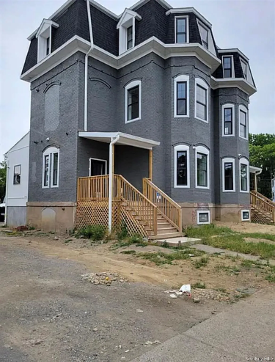 View of front of house with mansard roof, a porch, a shingled roof, and brick siding View of front of house with mansard roof, a porch, a shingled roof, and brick siding