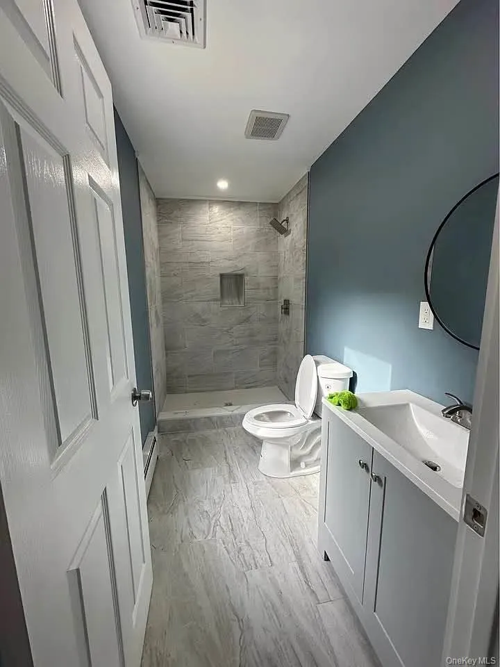 Bathroom featuring vanity, a stall shower, light wood-type flooring, and a baseboard heating unit Bathroom featuring vanity, a stall shower, light wood-type flooring, and a baseboard heating unit