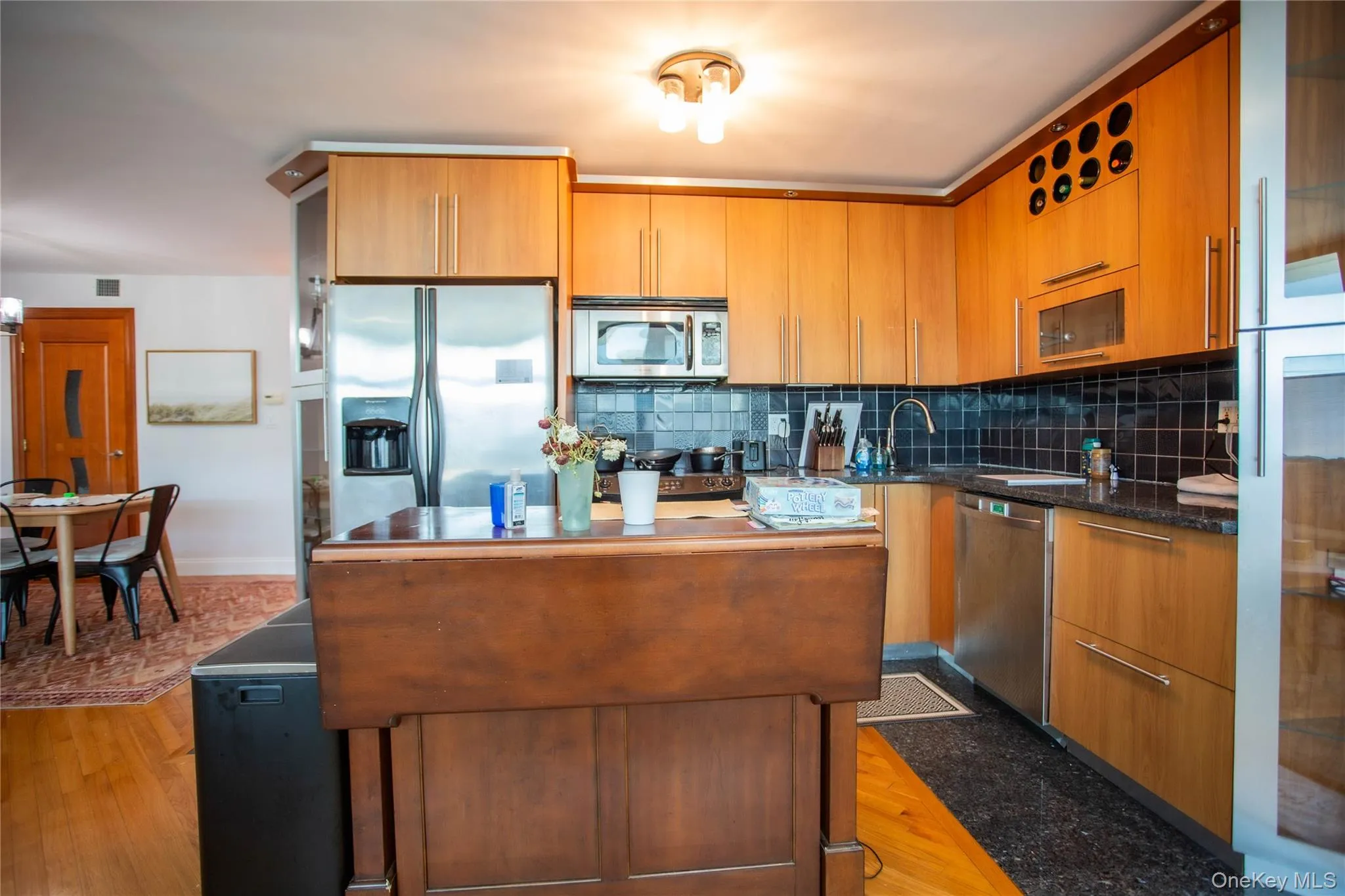 Kitchen featuring tasteful backsplash, appliances with stainless steel finishes, a center island, brown cabinetry, and light wood-type flooring Kitchen featuring tasteful backsplash, appliances with stainless steel finishes, a center island, brown cabinetry, and light wood-type flooring
