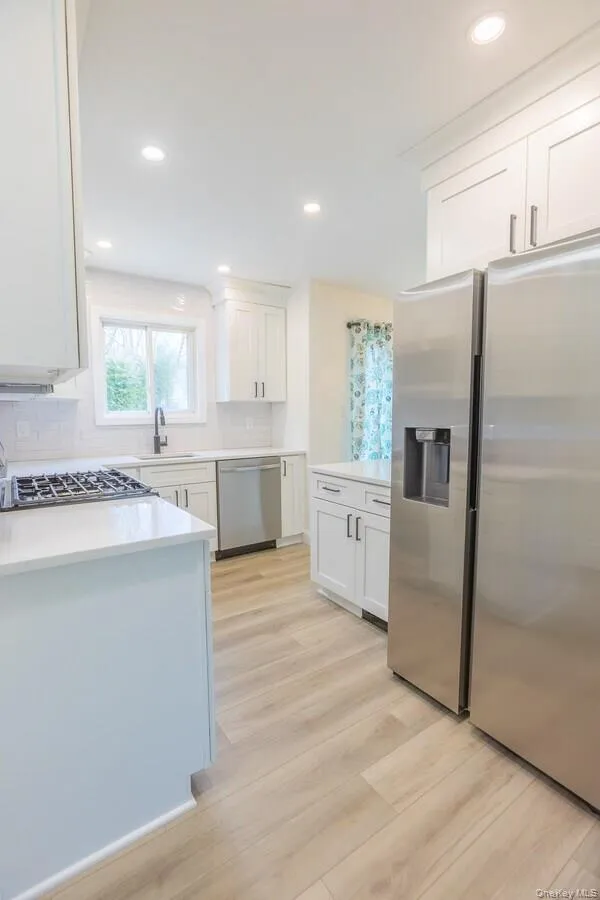 Kitchen featuring stainless steel appliances, white cabinetry, recessed lighting, backsplash, and light wood-style floors Kitchen featuring stainless steel appliances, white cabinetry, recessed lighting, backsplash, and light wood-style floors