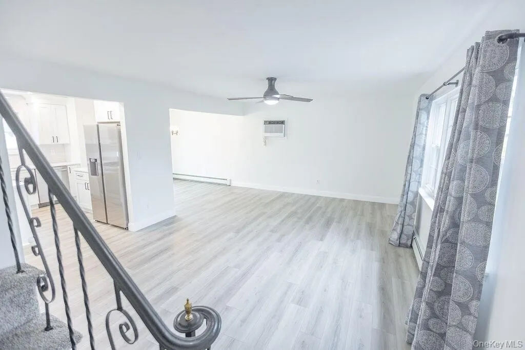Unfurnished living room with light wood-type flooring, a ceiling fan, baseboard heating, and an AC wall unit Unfurnished living room with light wood-type flooring, a ceiling fan, baseboard heating, and an AC wall unit