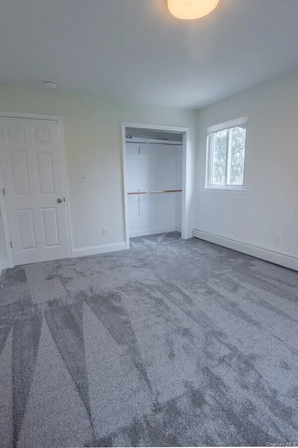 Unfurnished bedroom featuring carpet, a closet, and baseboard heating Unfurnished bedroom featuring carpet, a closet, and baseboard heating