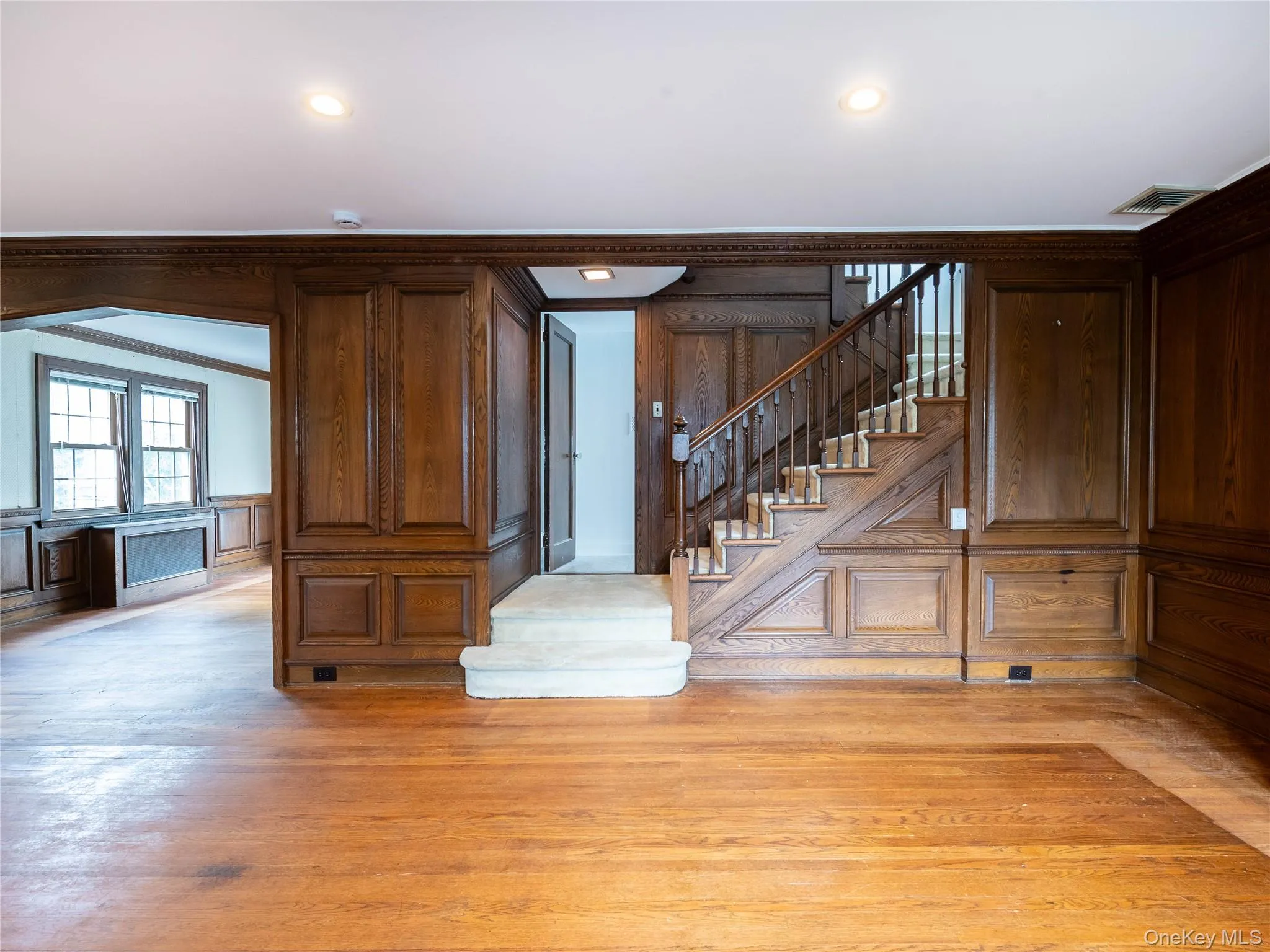 Stairway featuring wood finished floors, crown molding, and a decorative wall Stairway featuring wood finished floors, crown molding, and a decorative wall