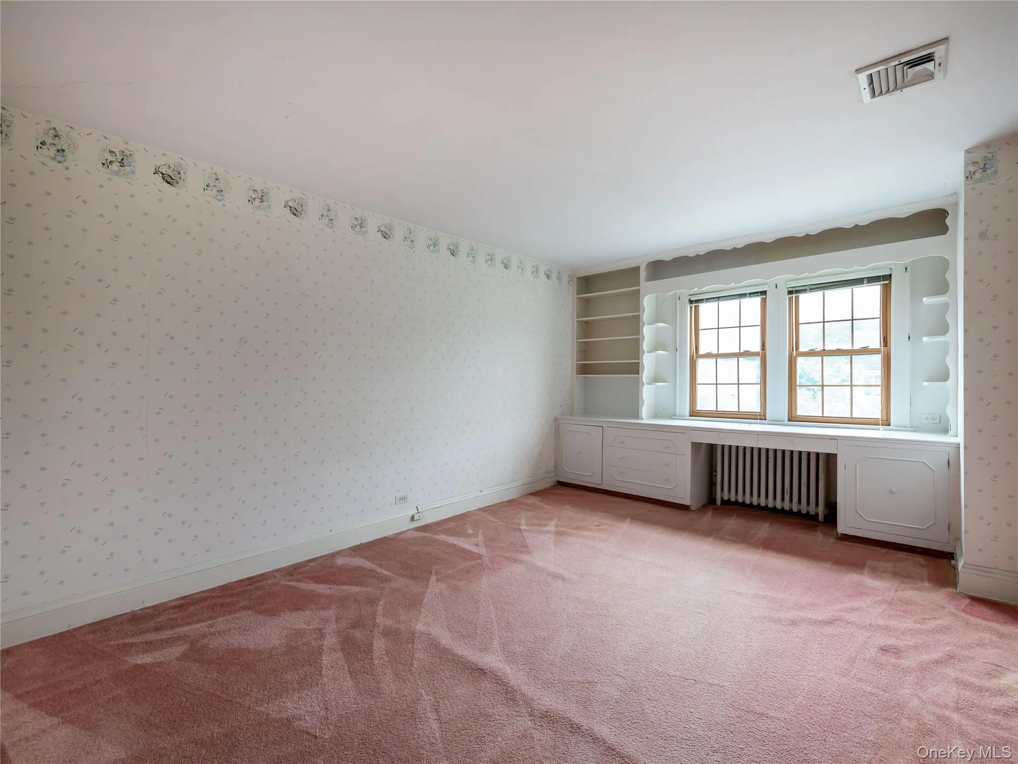 Spare room with wallpapered walls, light colored carpet, and radiator heating unit Spare room with wallpapered walls, light colored carpet, and radiator heating unit