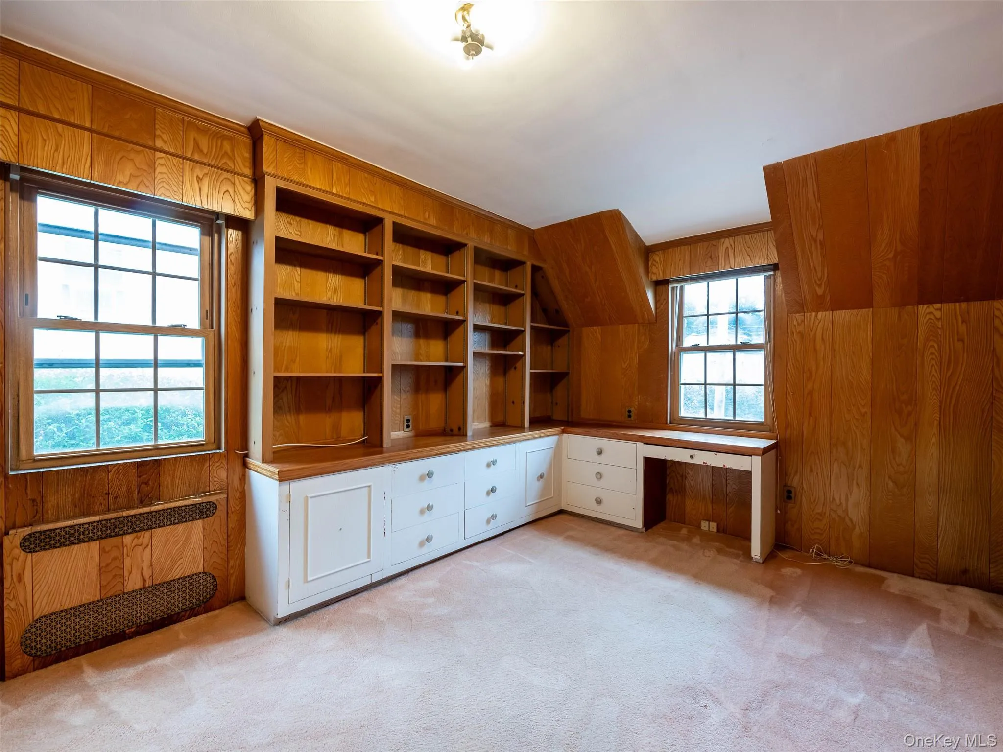 Unfurnished office with wooden walls, built in study area, and light carpet Unfurnished office with wooden walls, built in study area, and light carpet